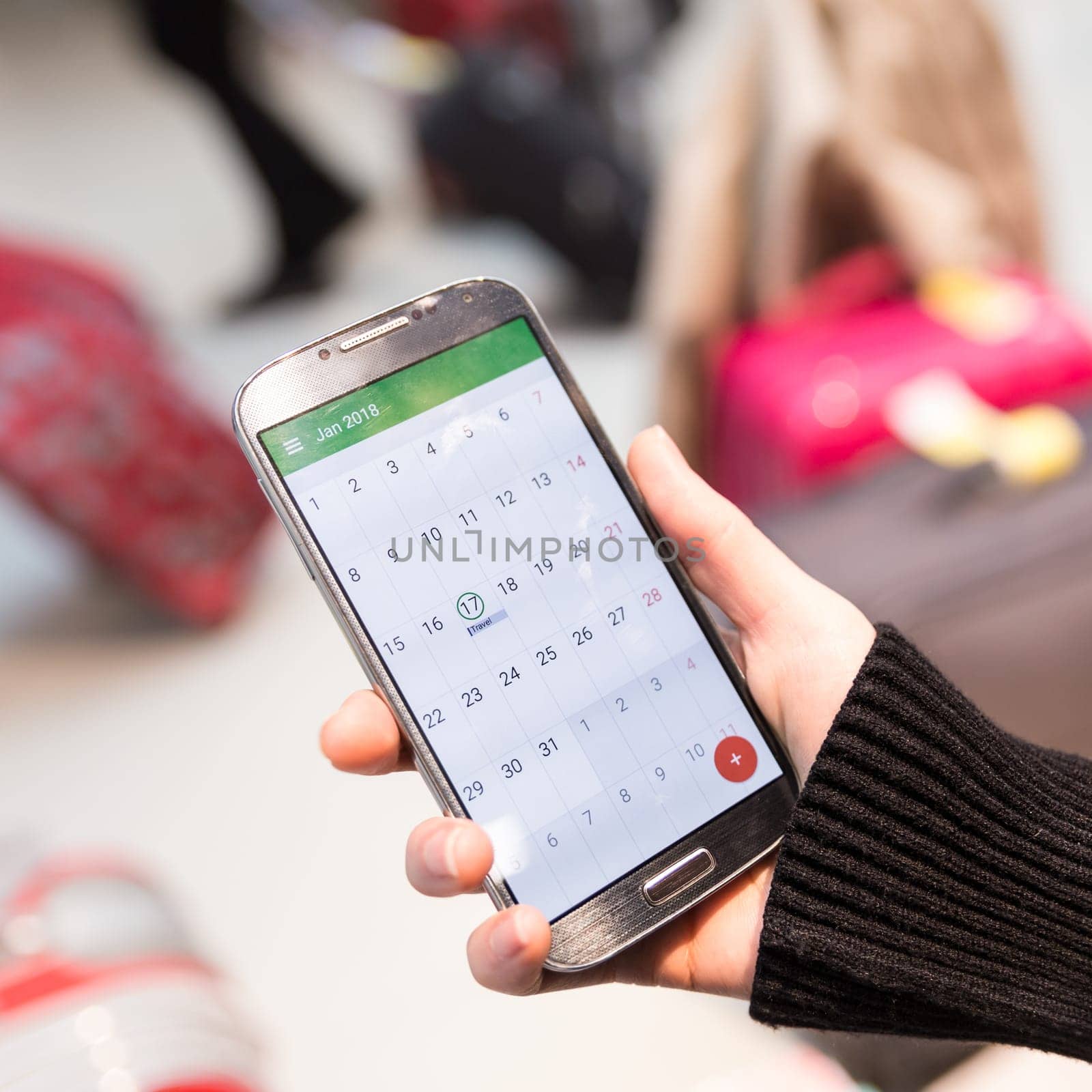 Woman checking calendar information on mobile phone sitting in airport terminal. Concept of people sharing informations with new technology while traveling. Selective focus on smart phone, close up.