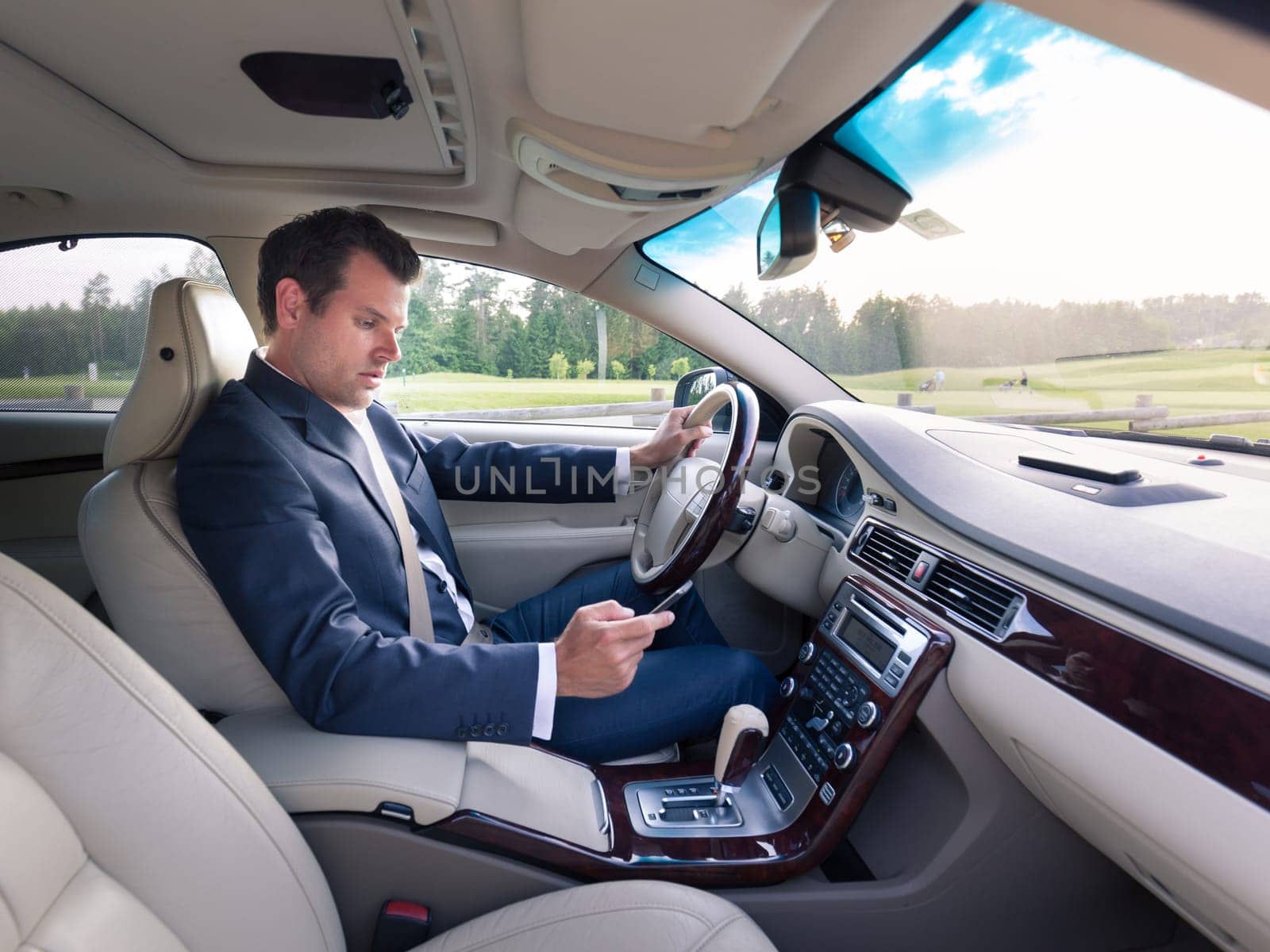 Businessman using cell phone and texting while driving not paying attention to the road. Dangerous texting and driving at the same time