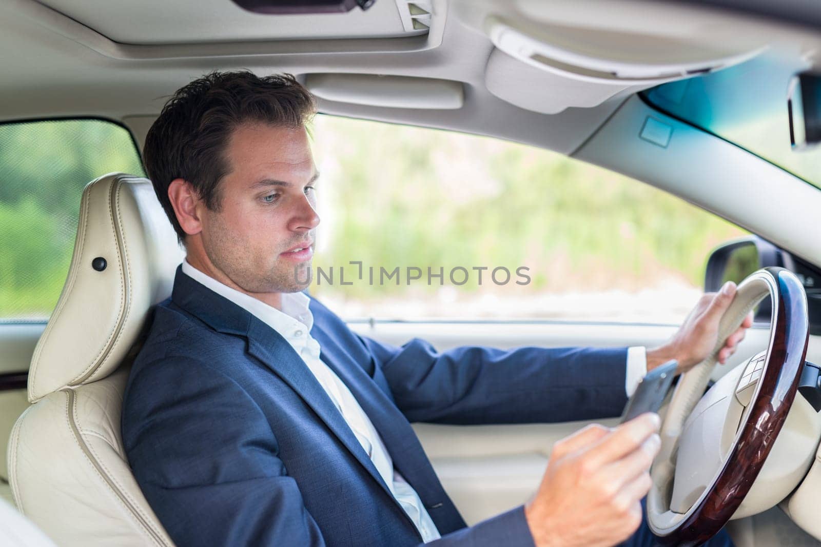 Businessman using cell phone and texting while driving not paying attention to the road. Dangerous texting and driving at the same time