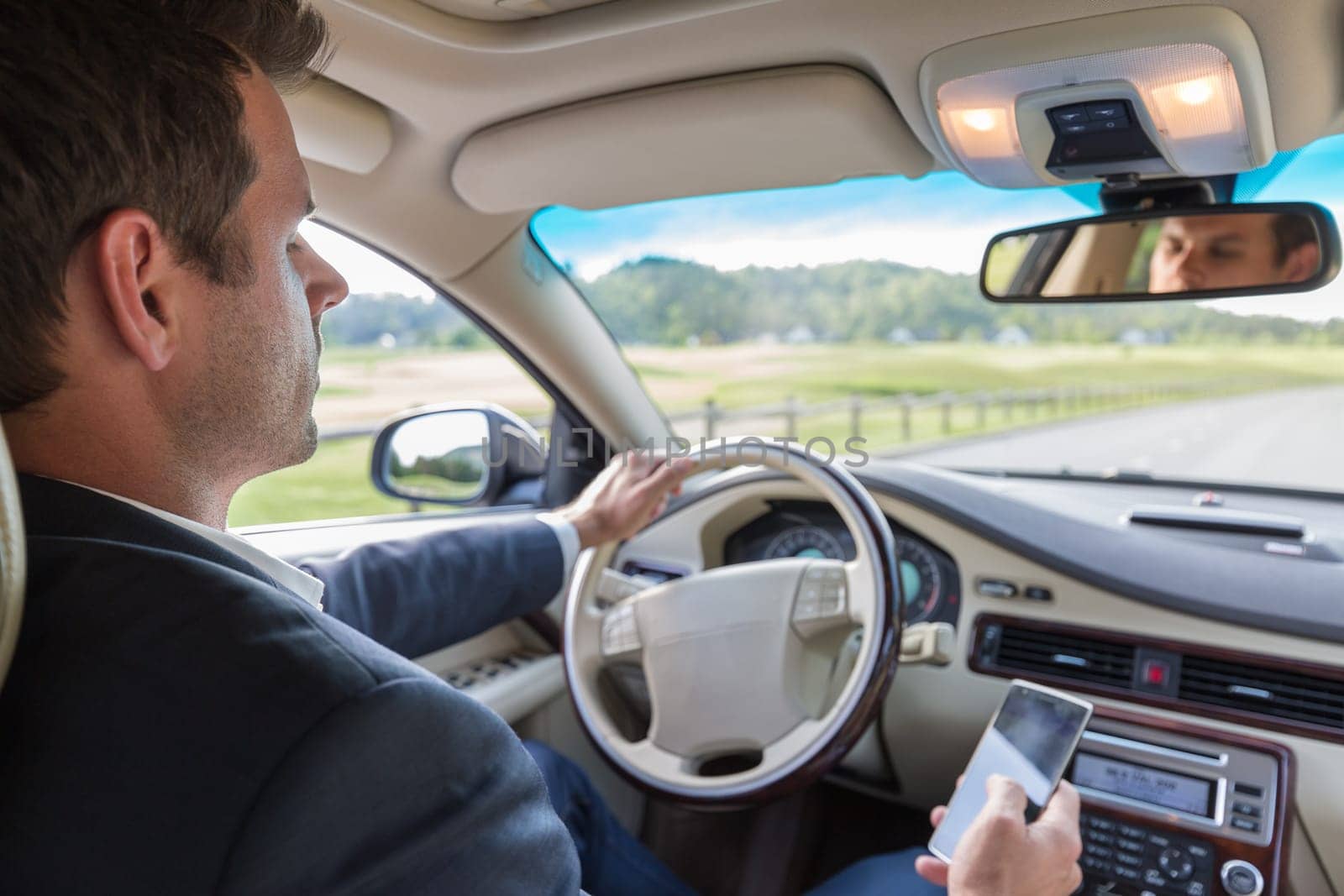 Businessman using cell phone and texting while driving not paying attention to the road. Dangerous texting and driving at the same time