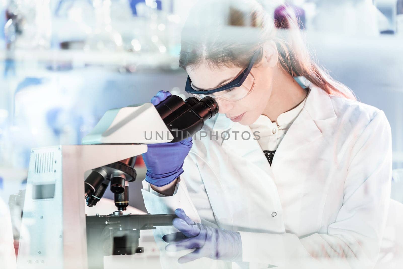 Life scientists researching in laboratory. Attractive female young scientist microscoping in their working environment. Healthcare and biotechnology.