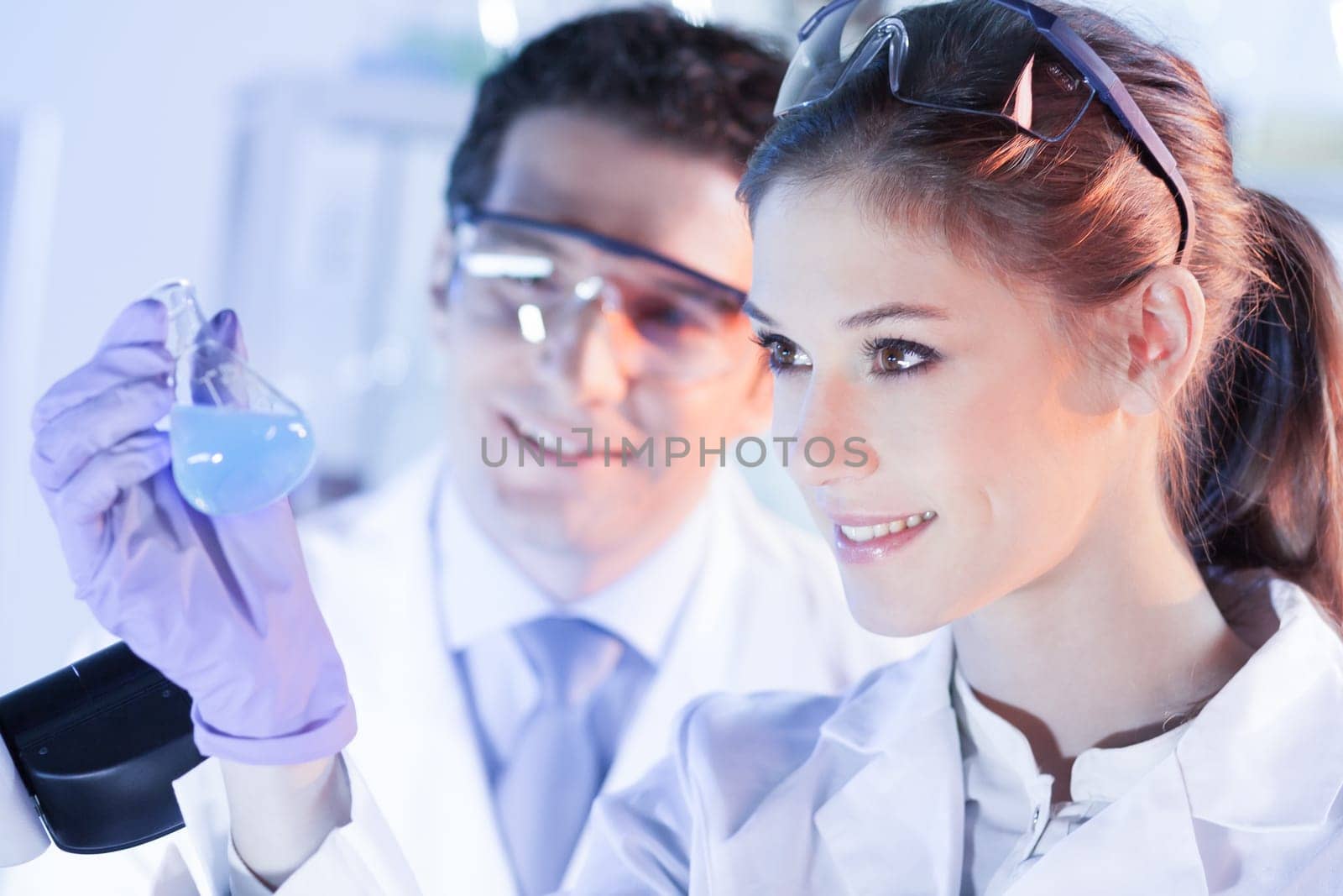 Chemical laboratory. Attractive young PhD student and her post doctoral supervisor scientist observing the blue indicator color shift after the solution destillation.