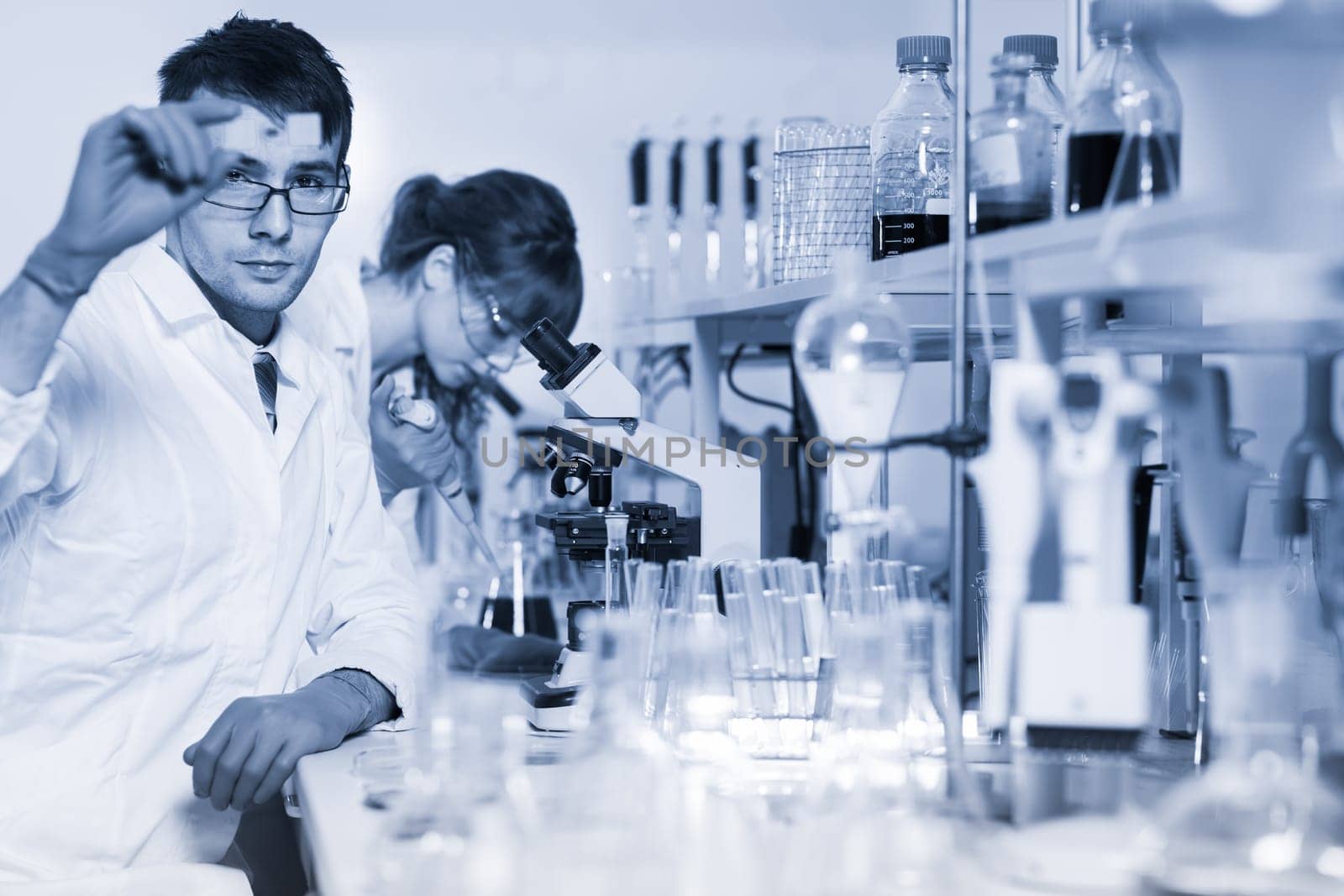 Health care researchers working in life science laboratory. Young researchs preparing and analyzing microscope slides in research lab.