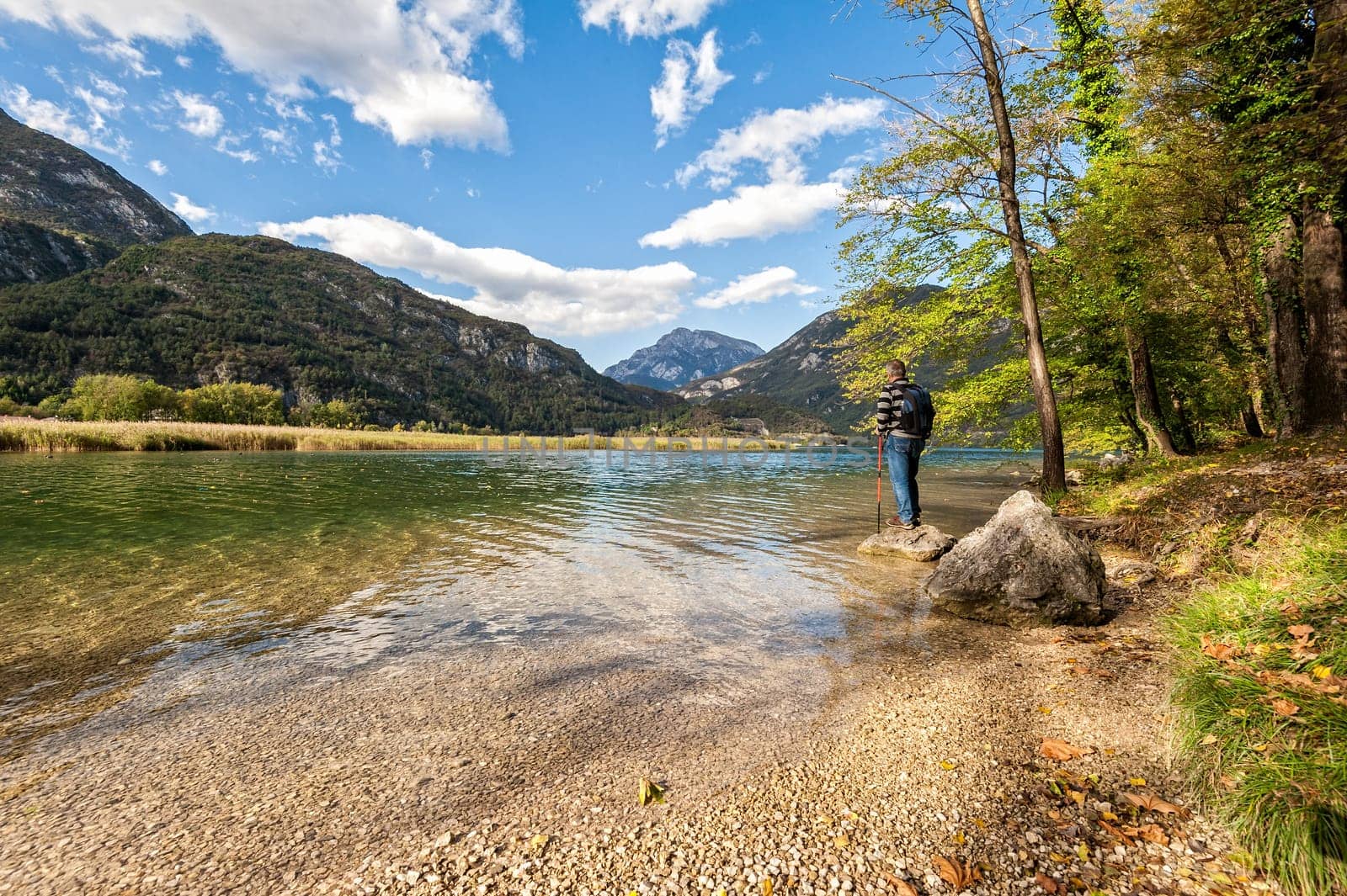 Hiker standing on the shore of the lake among the mountains admiring the landscape.