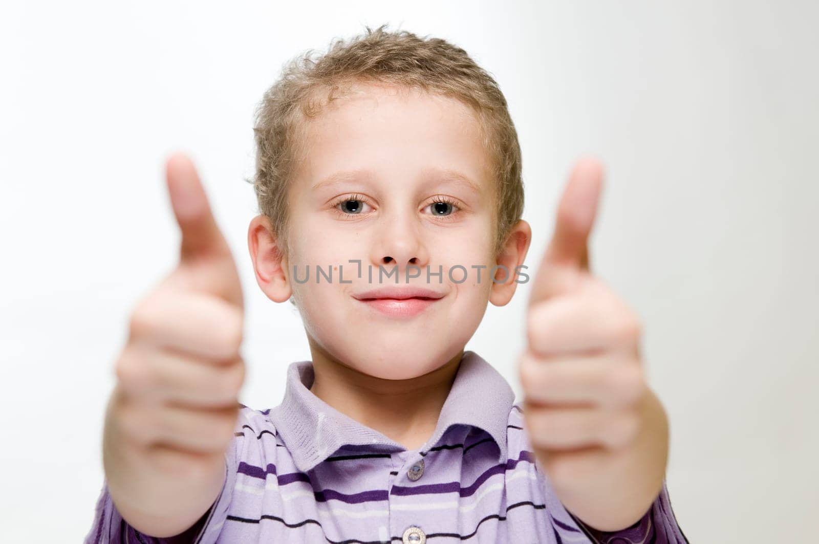 Upper body view of a seven-year-old boy against a white background pointing two thumbs up.