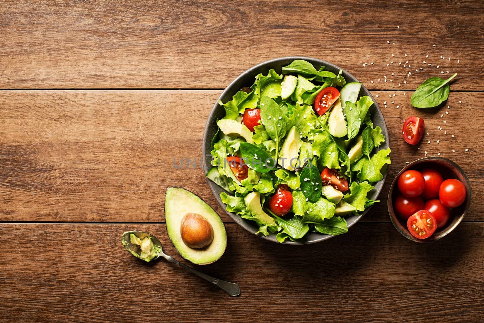 Green salad with avocado and fresh vegetables on wooden background.
