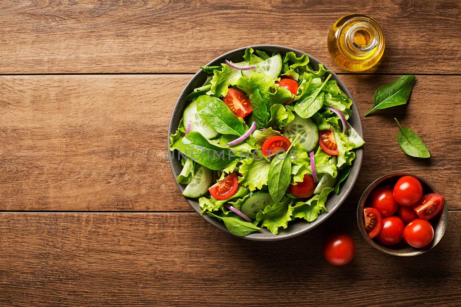 Green salad with tomato and fresh vegetables on a wooden background