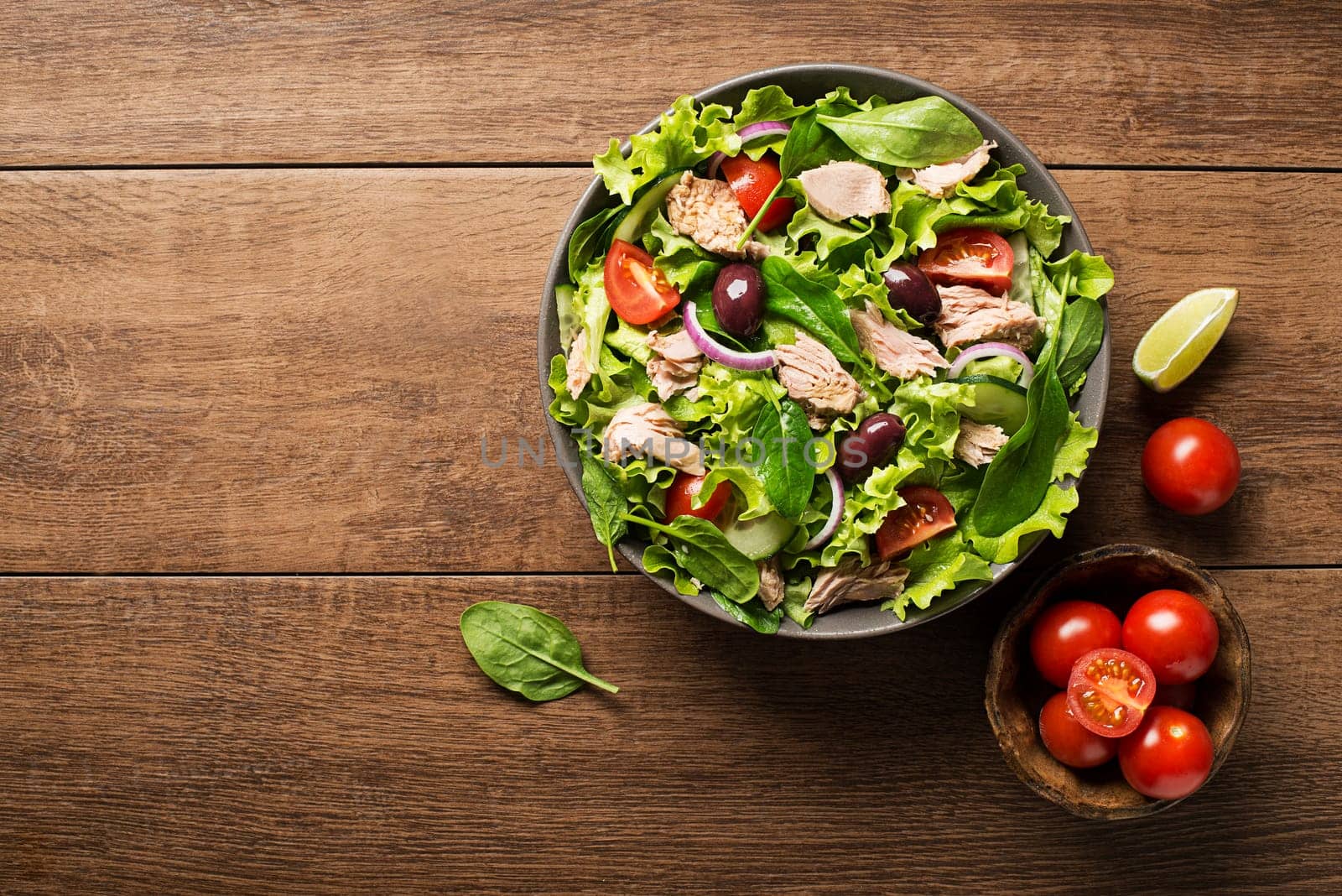 Tuna salad with lettuce, tomatoes and olives on wooden table