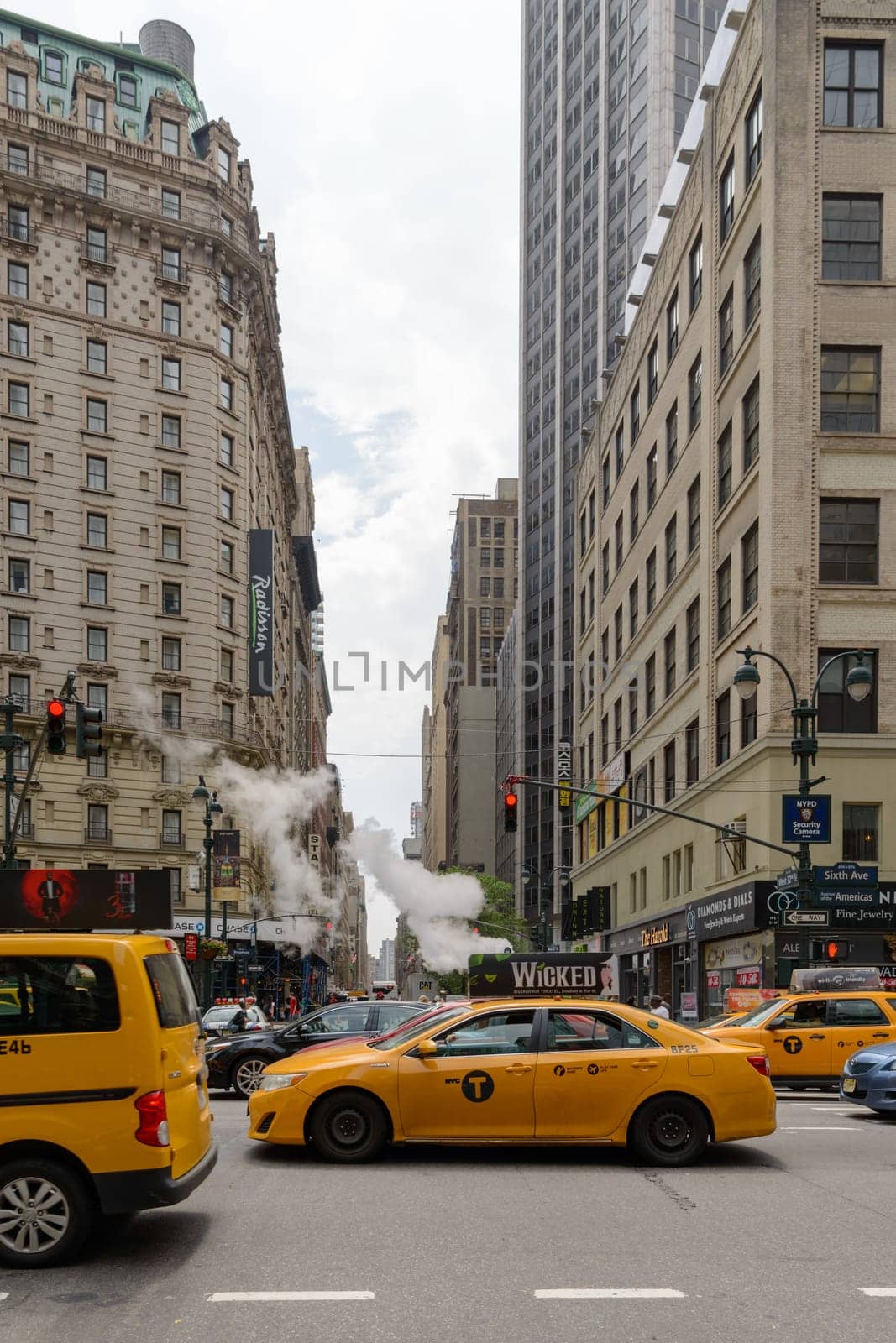 New York, NY, USA - June 06, 2015:Steam coming out of Greeley Square and the intersection West 32 in Manhattan in the spring. Traffic of cars and crowds of people.