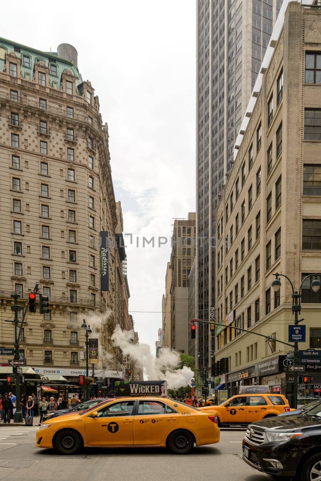 New York, NY, USA - June 06, 2015:Steam coming out of Greeley Square and the intersection West 32 in Manhattan in the spring. Traffic of cars and crowds of people.