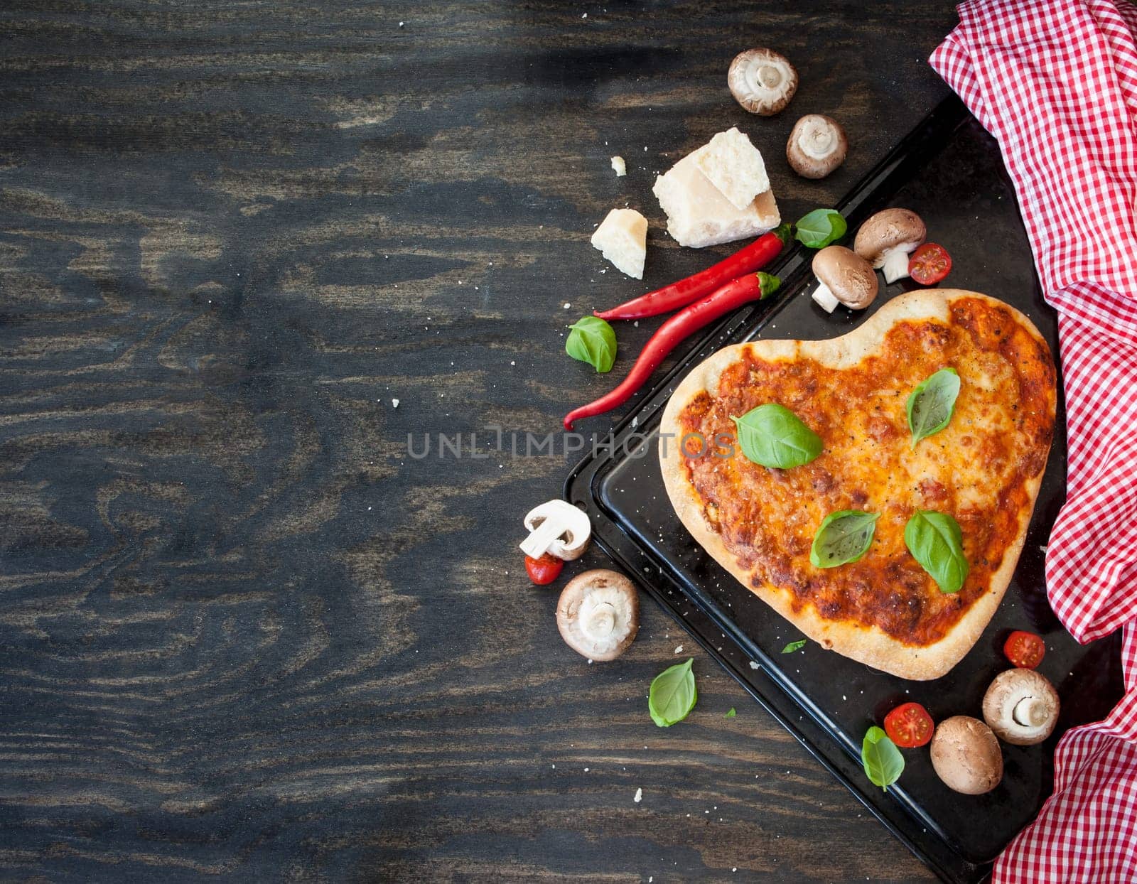 Heart-shaped pizza Margherita with fresh ingredients on a rustic wooden background
