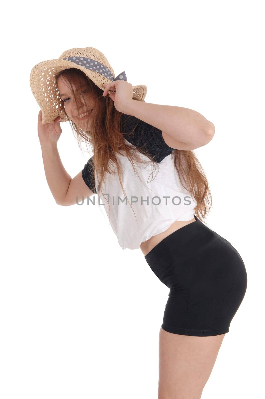 A smiling young woman wearing a straw hat and black shorts bending.forwards and smiling, isolated for white background.