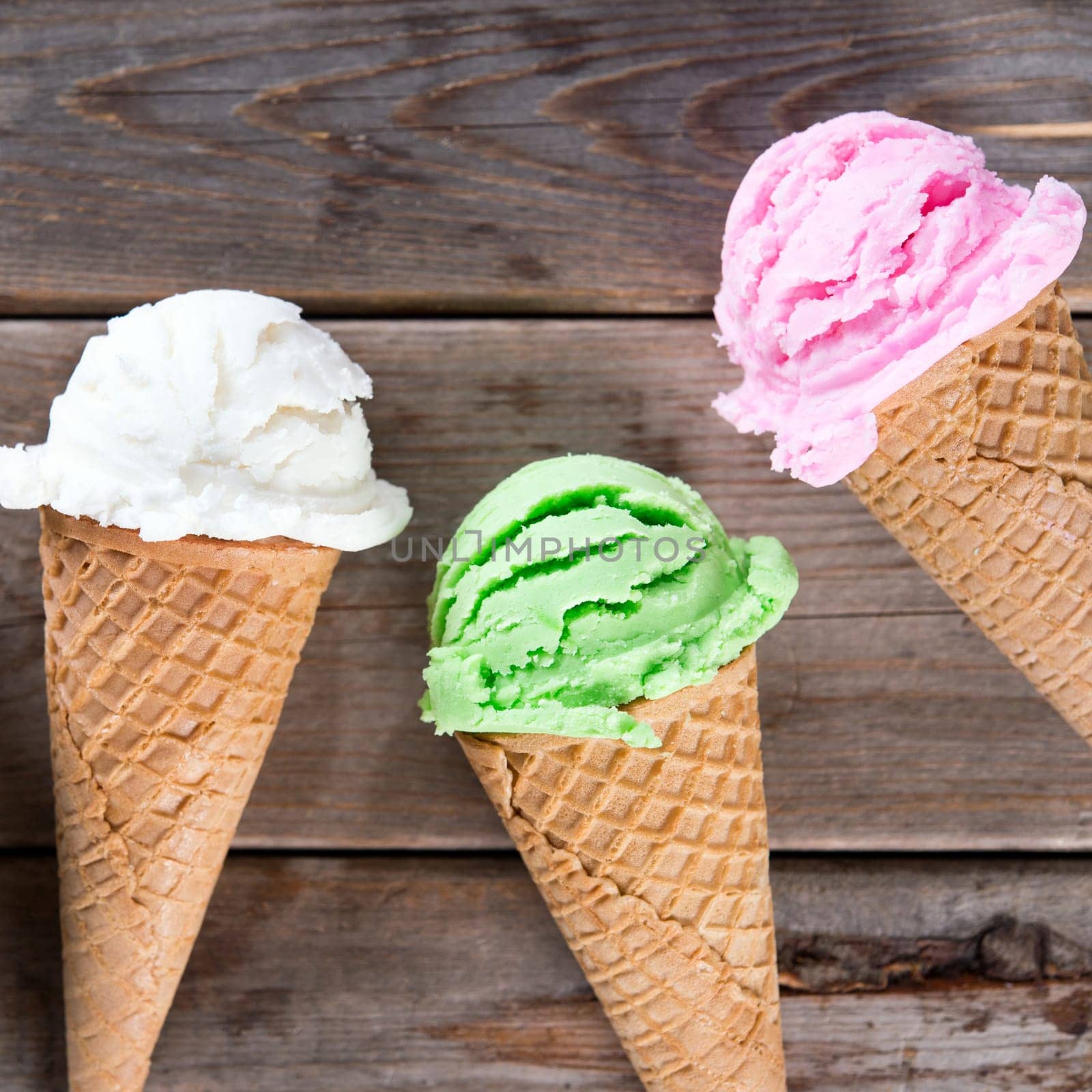 Top view vanilla, matcha and strawberry ice cream in the cone on old rustic wooden vintage background.