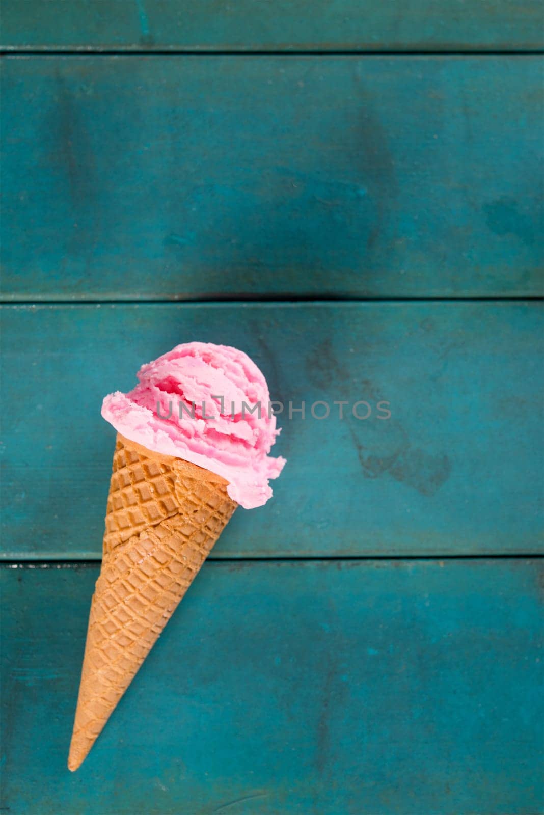 Top view strawberry ice cream waffle cone on blue wooden background, close up.