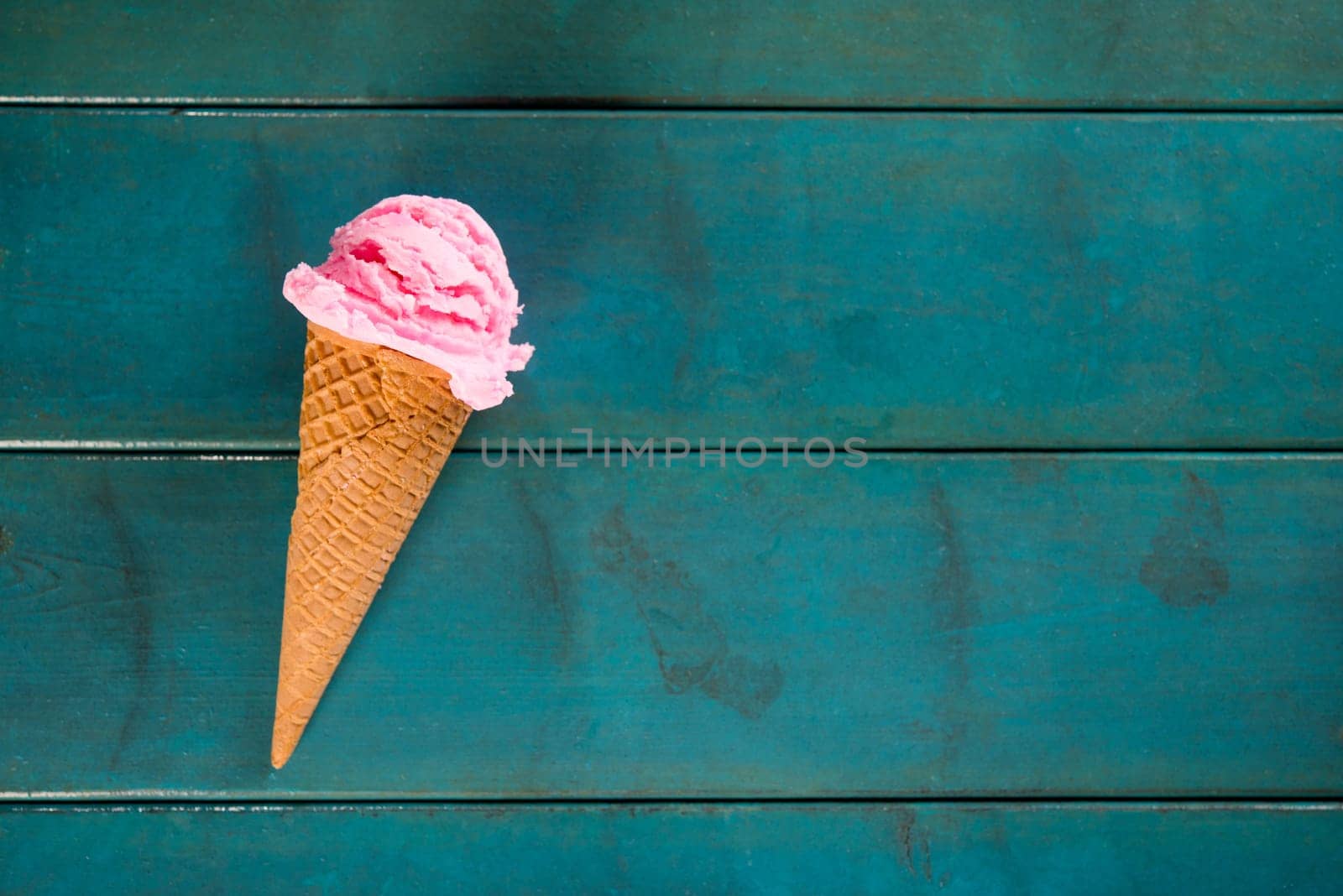 Top view strawberry ice cream waffle cone on blue wooden background, copy space on side.