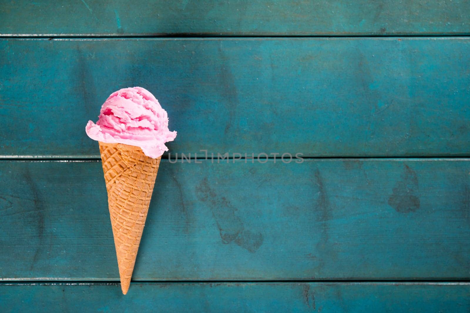 Top view strawberry ice cream waffle cone on blue wooden background, copy space on side.