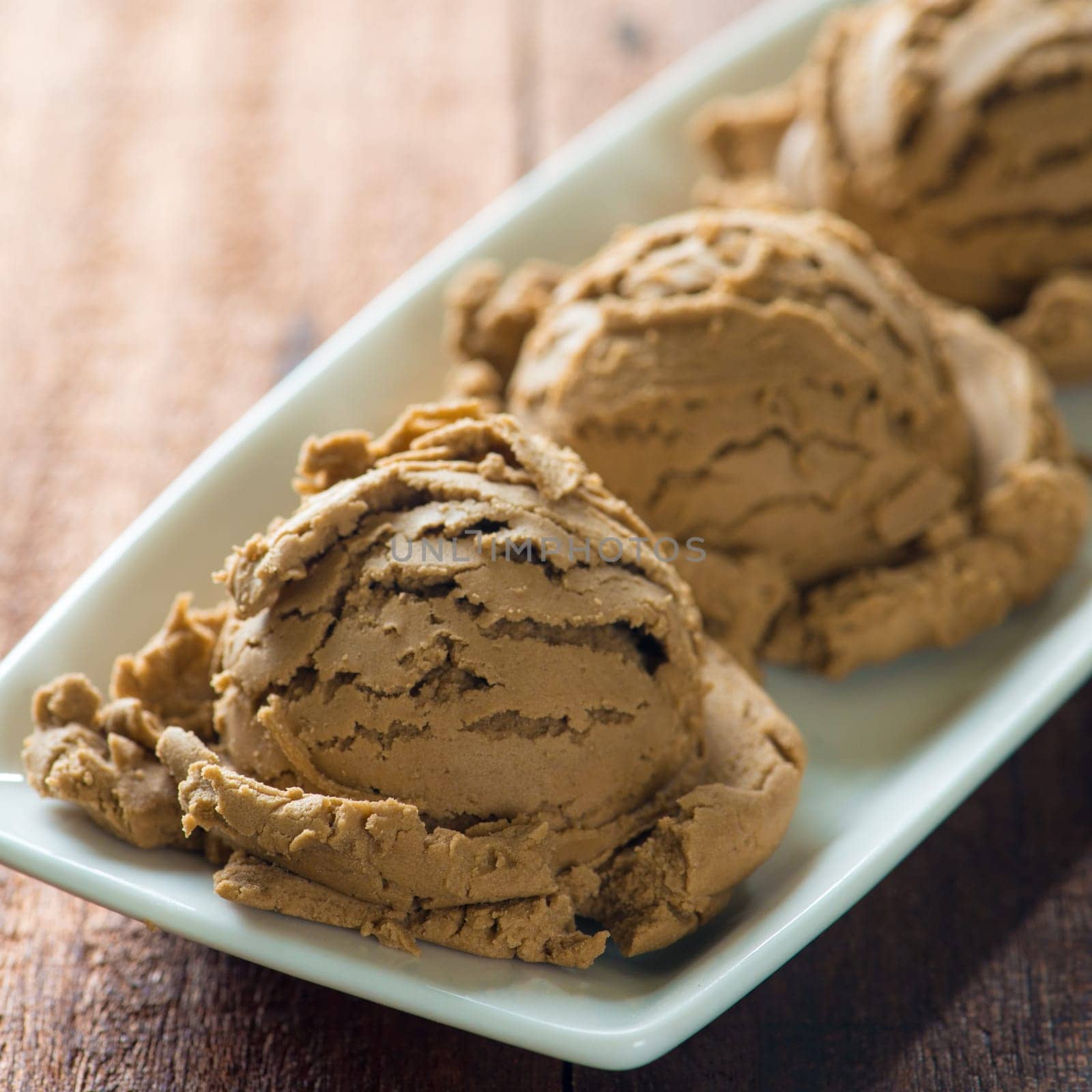 Brown ice cream in plate on dark wooden background.
