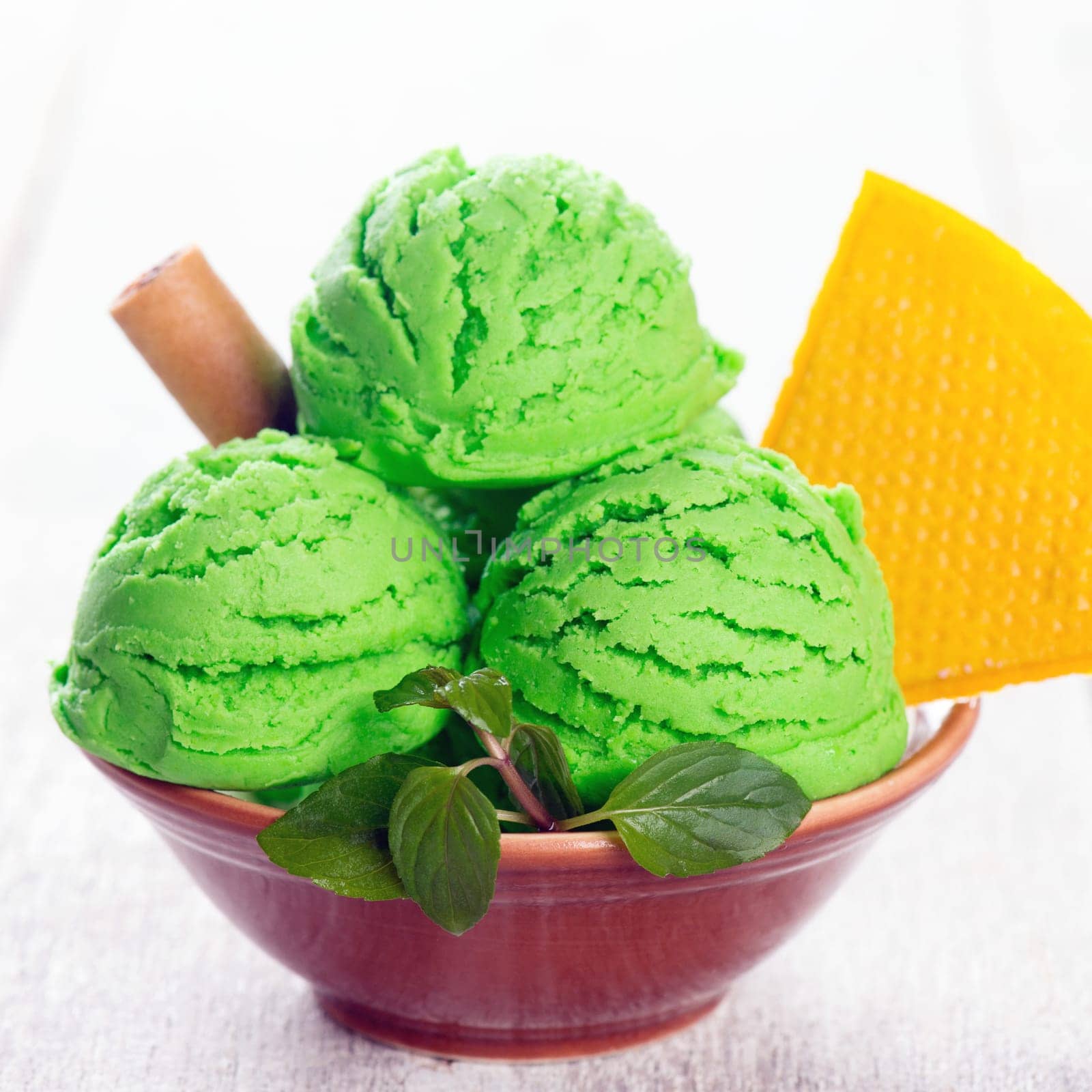 Scoop of green ice cream in bowl on wooden background.