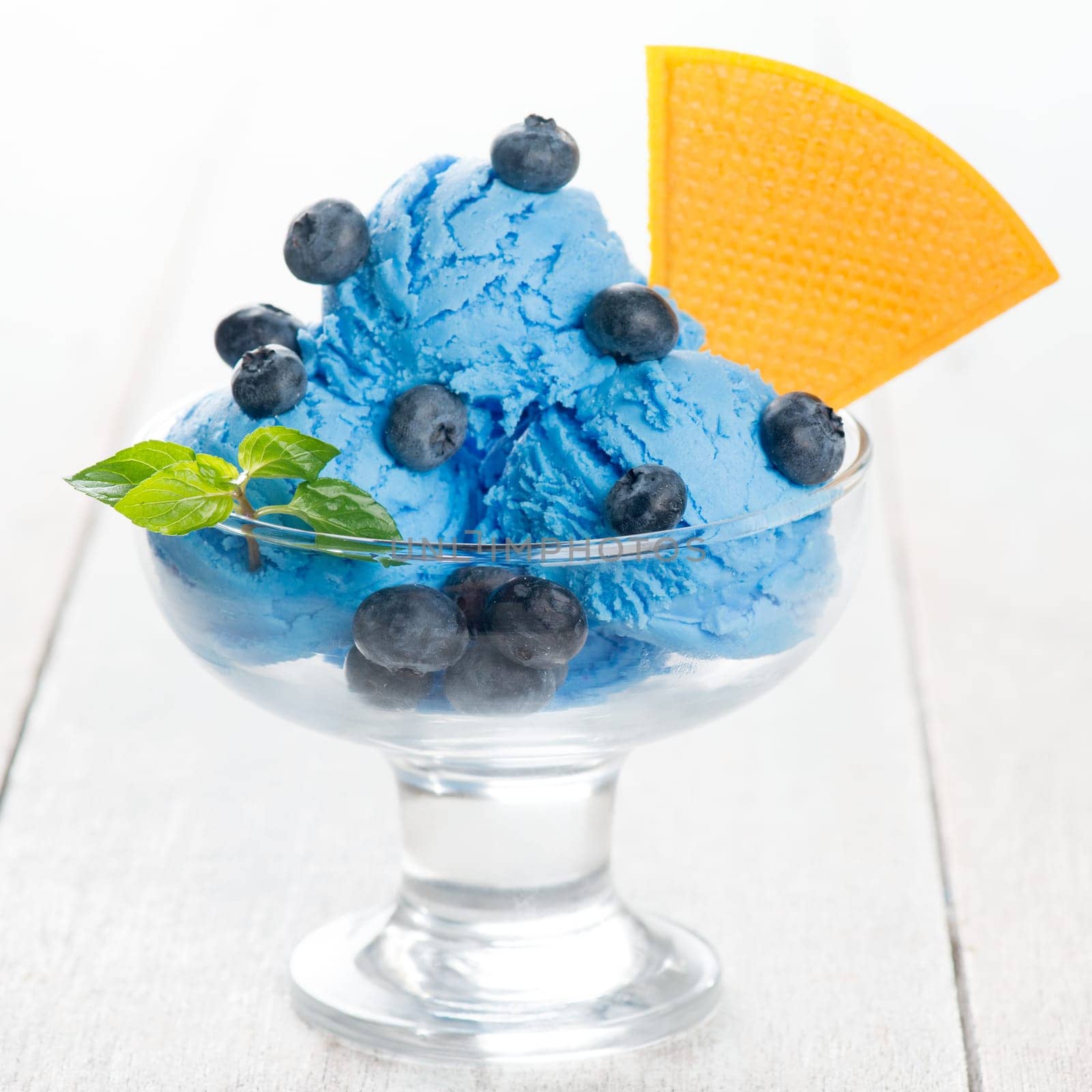 Blue ice cream in cup with blueberry fruits on white wooden background.