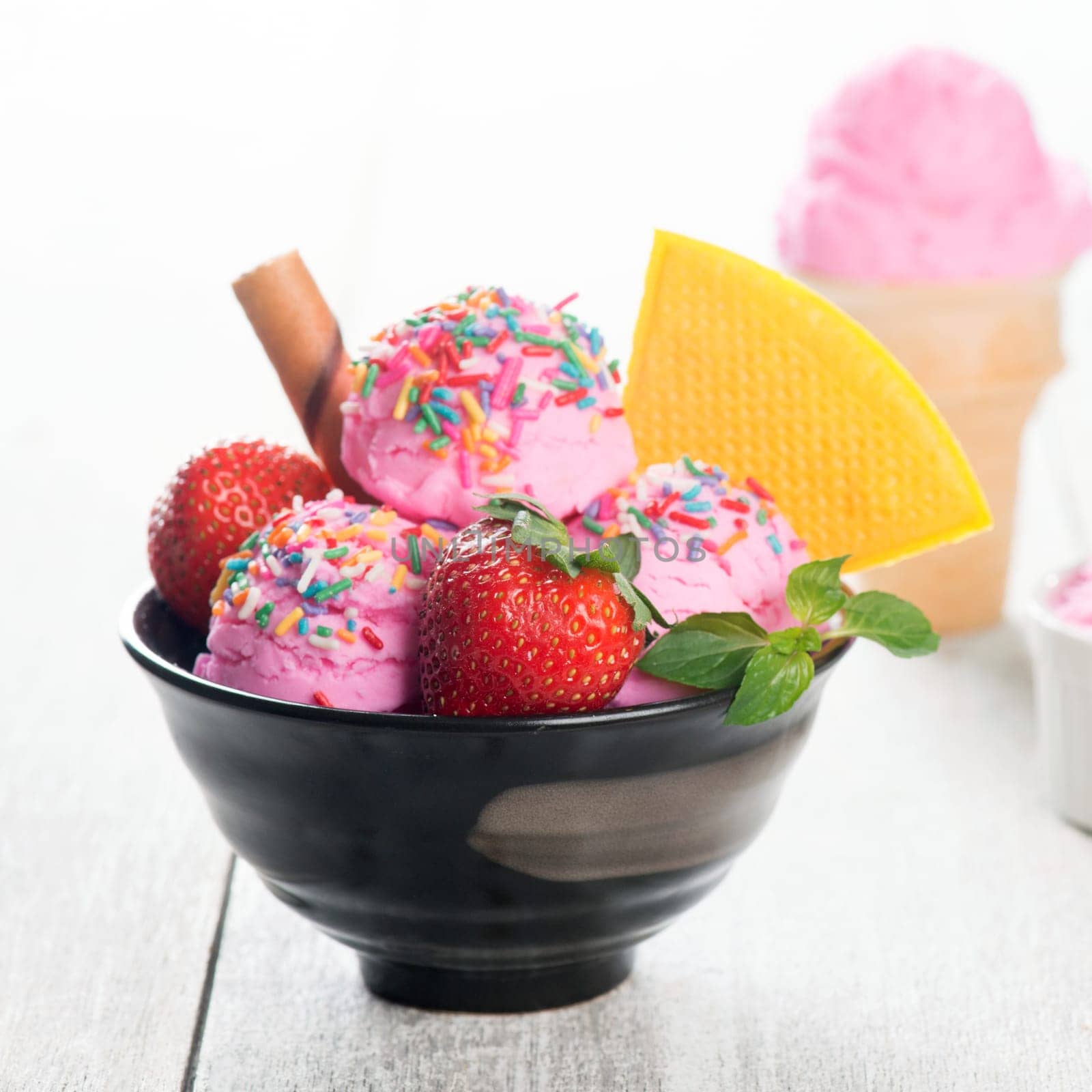 Pink ice cream in bowl with strawberry fruits and waffle on white rustic wooden background.