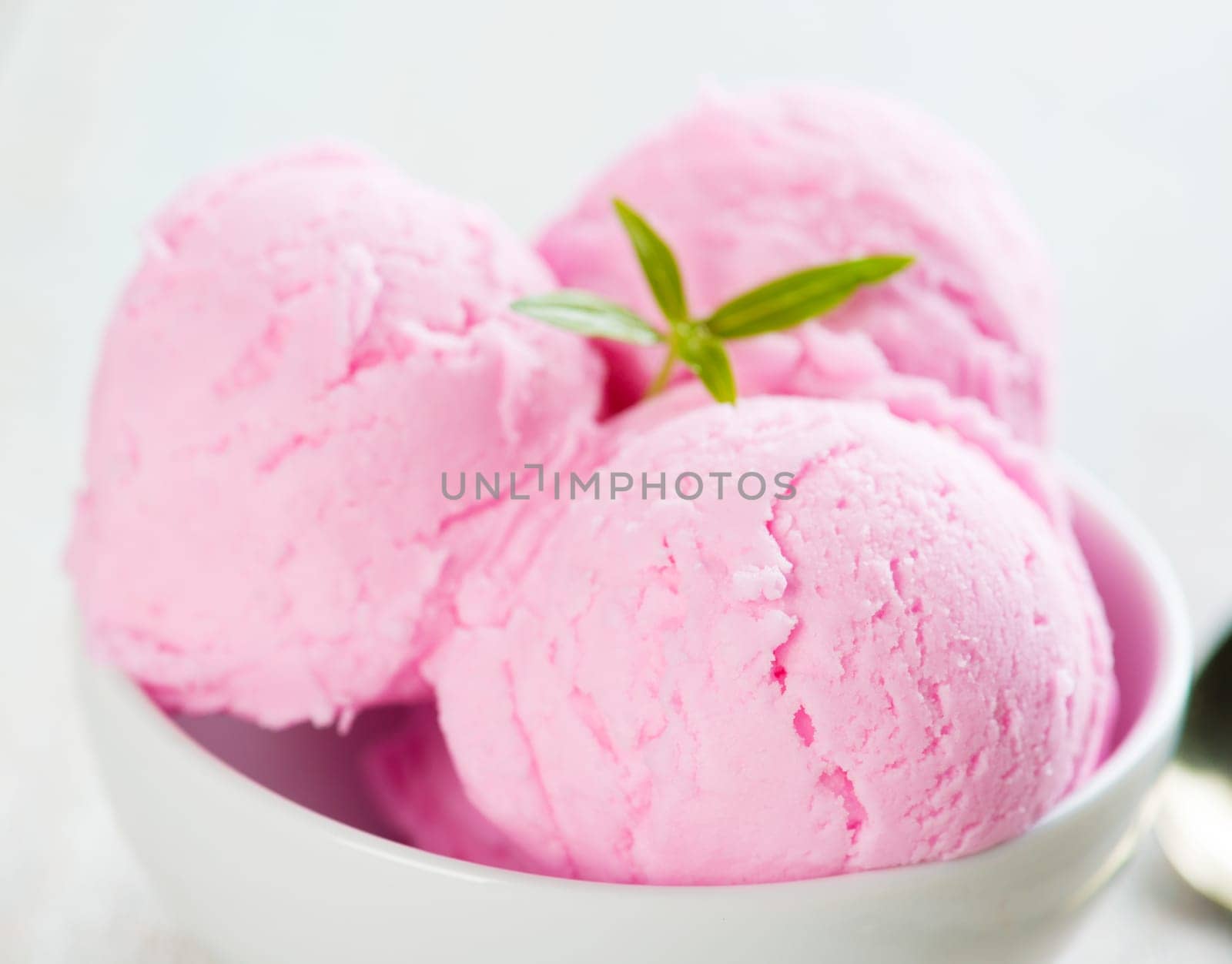 Pink berry ice cream in bowl on white wooden background.
