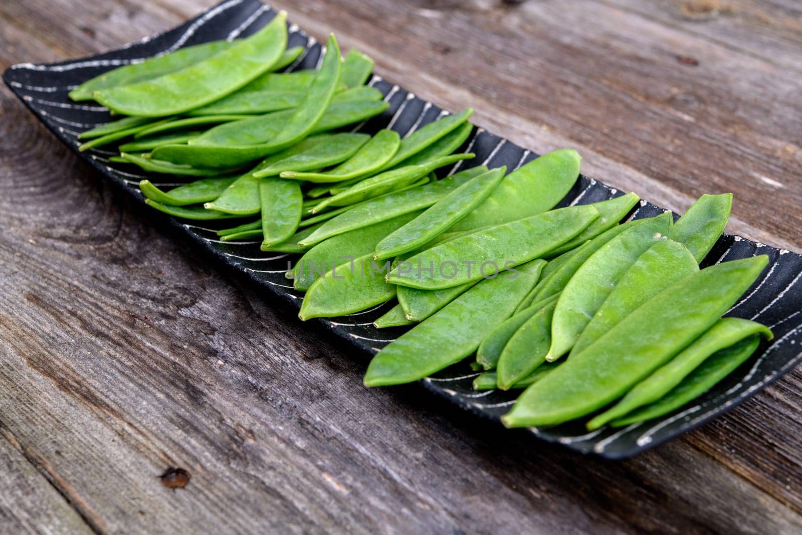 elongated bowl with green peapods  on wooden ground