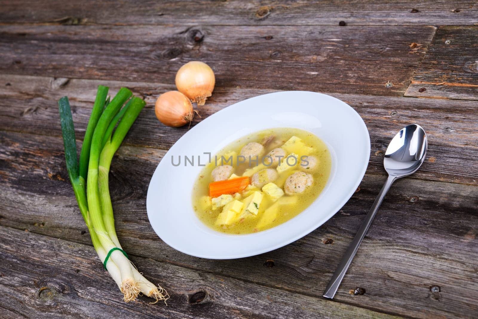 marrow balls soup in white plate with onion on wooden ground