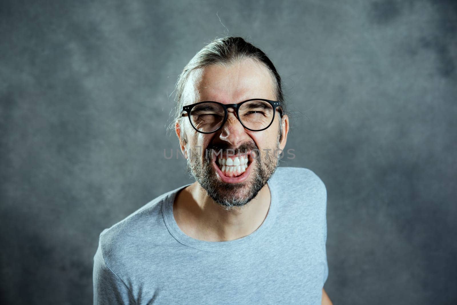 young man in front of gray background looking angry