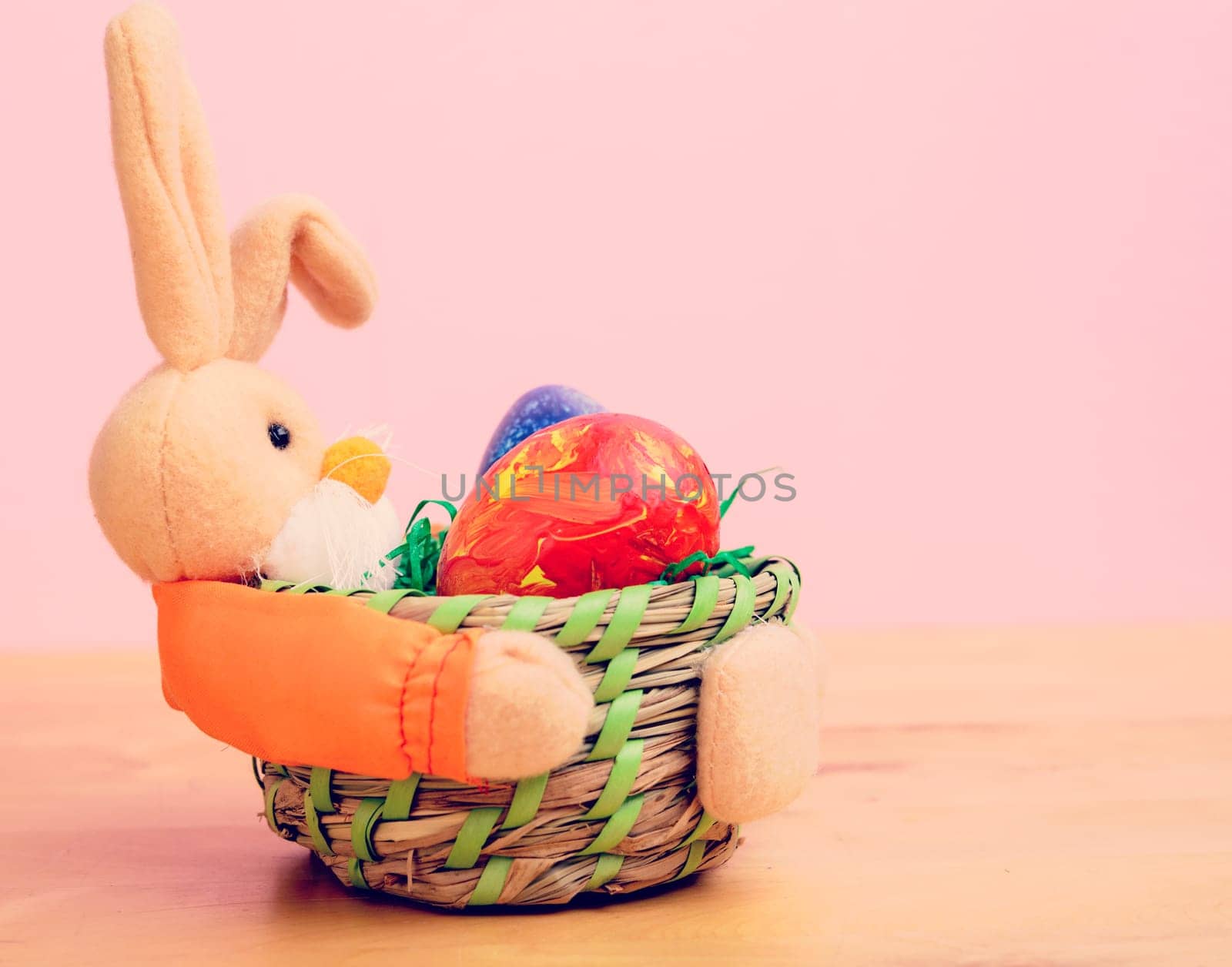 easter bunny in basket with egg in front of pink background