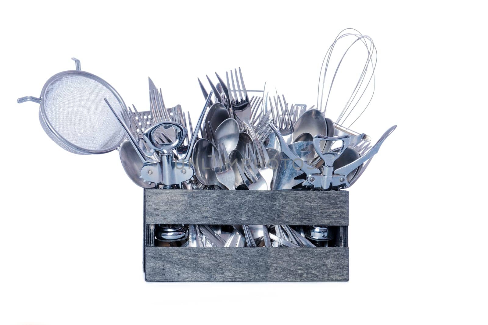 Wooden box filled with stainless steel kitchen cutlery. White cutout background.