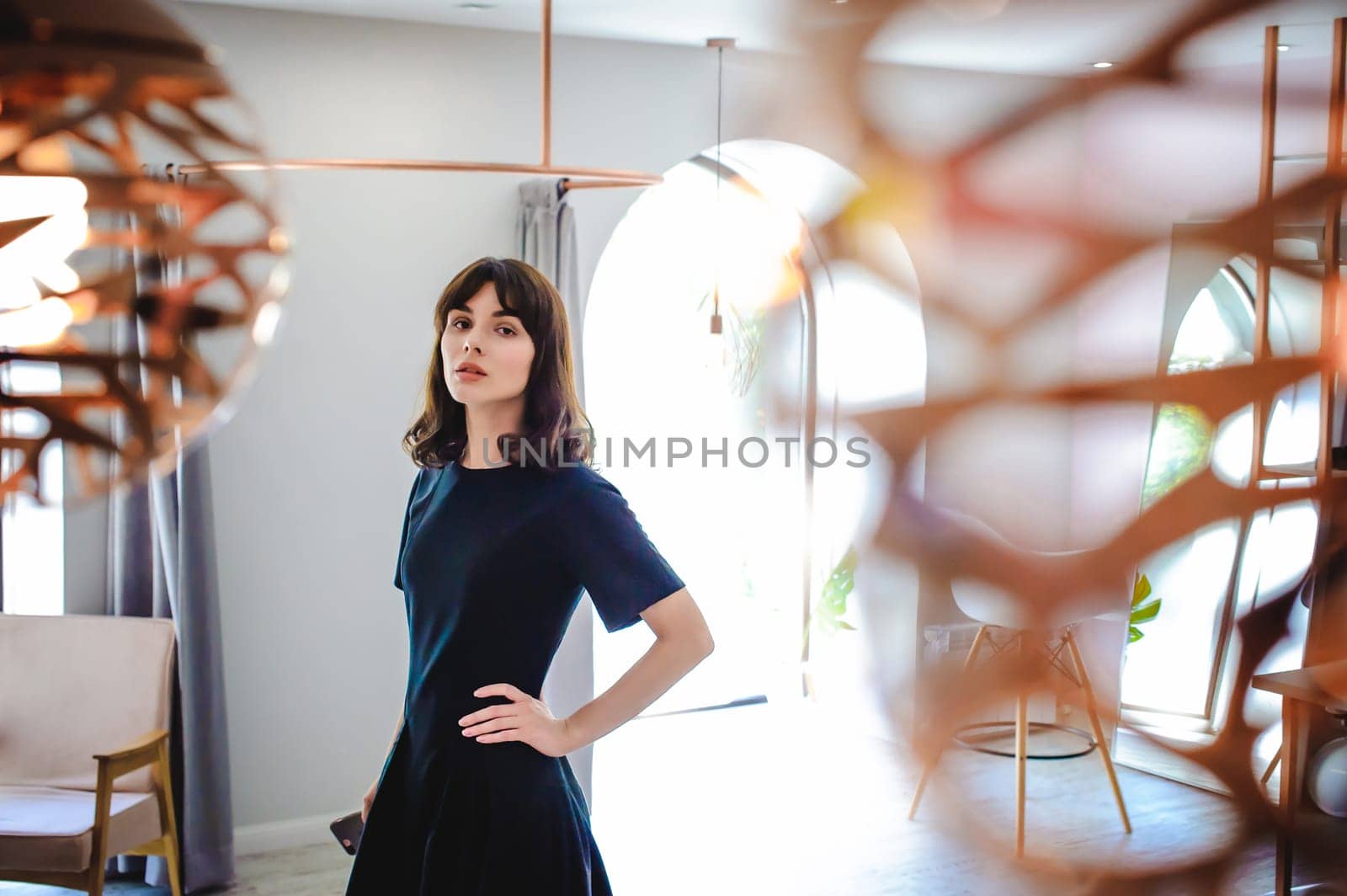 young woman in an elegant black dress with a phone in her hand, into a room with a pink interior and a fashionable lamp