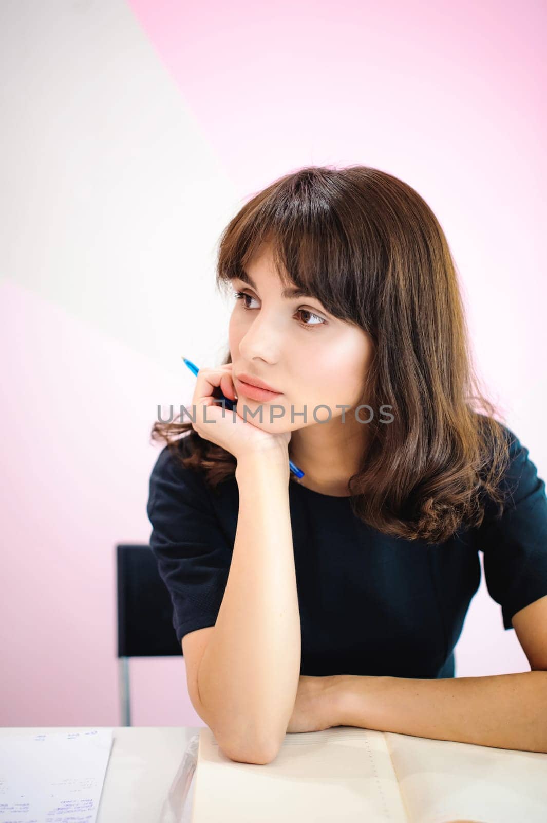 Portrait of a beautiful business woman making notes in a notebook. Holds a pen, sitting in the workplace in a pink office