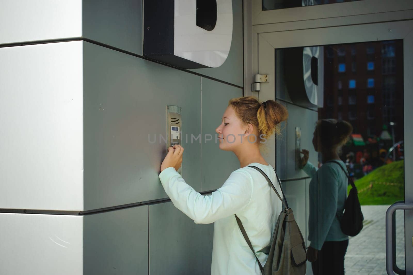 young blond teenager schoolgirl dials the code for a call over the intercom
