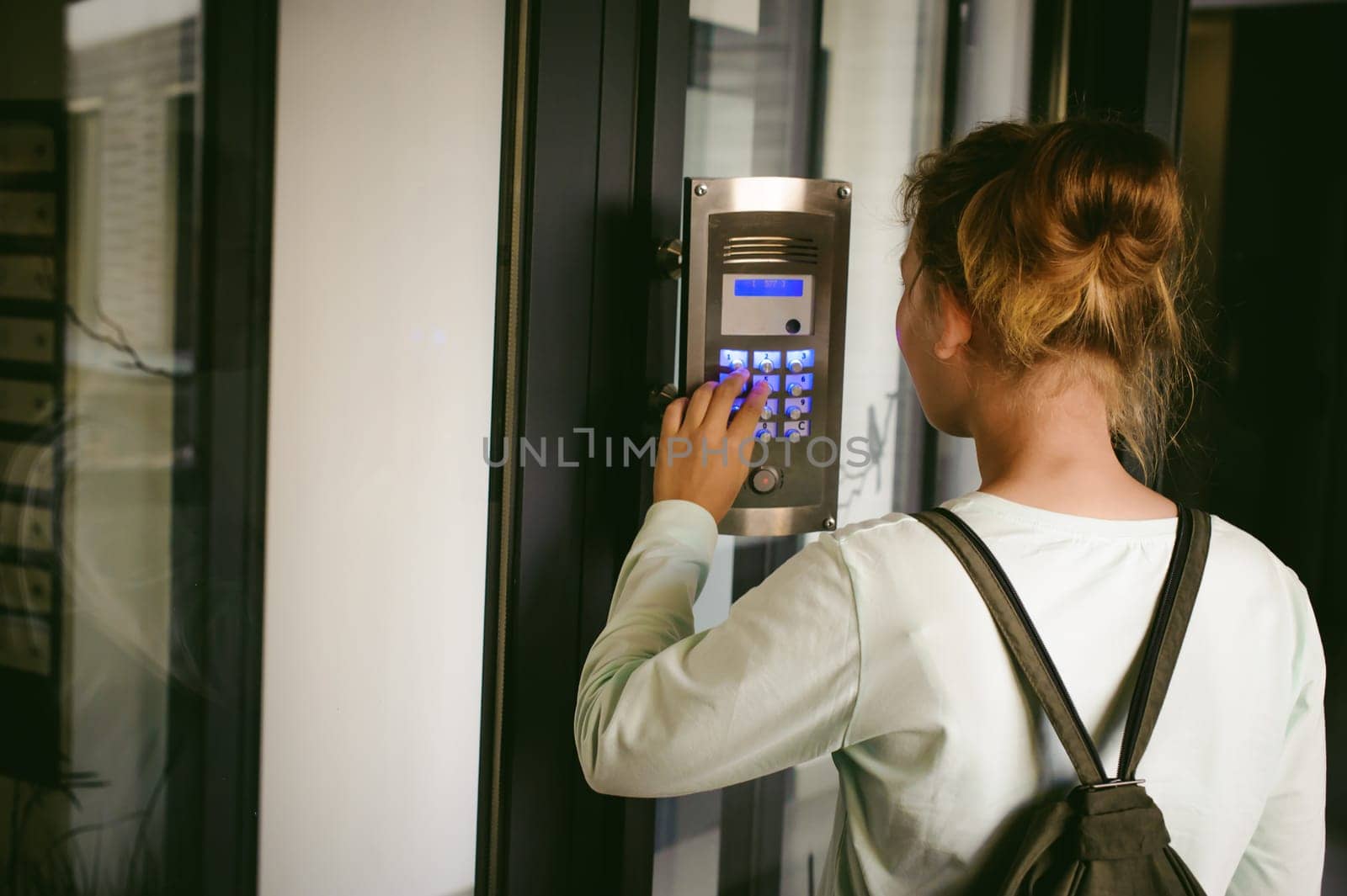 young blond teenager schoolgirl dials the code for a call over the intercom