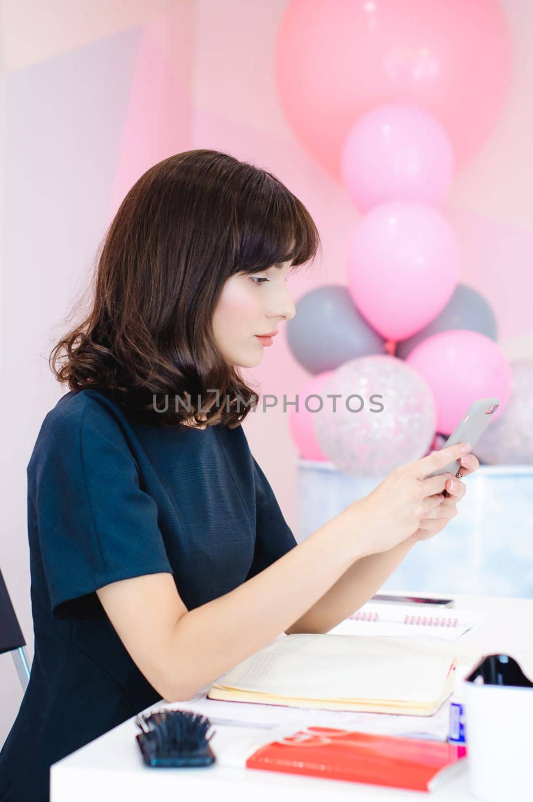 Portrait of a beautiful business woman making notes in a smartphone. Holding a cell phone while sitting in a workplace in a pink office