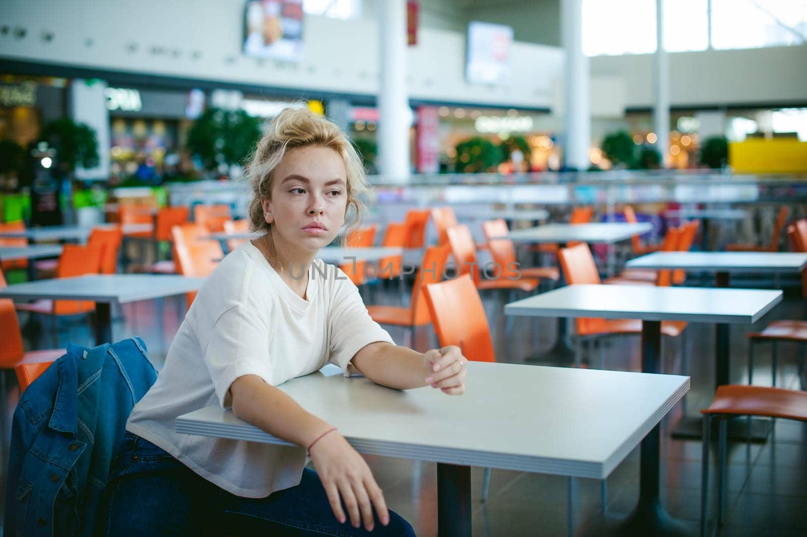 young beautiful woman in jeans clothes in business space of shopping center. portrait of a girl with freckles on her face, stylish girl in an empty cafe