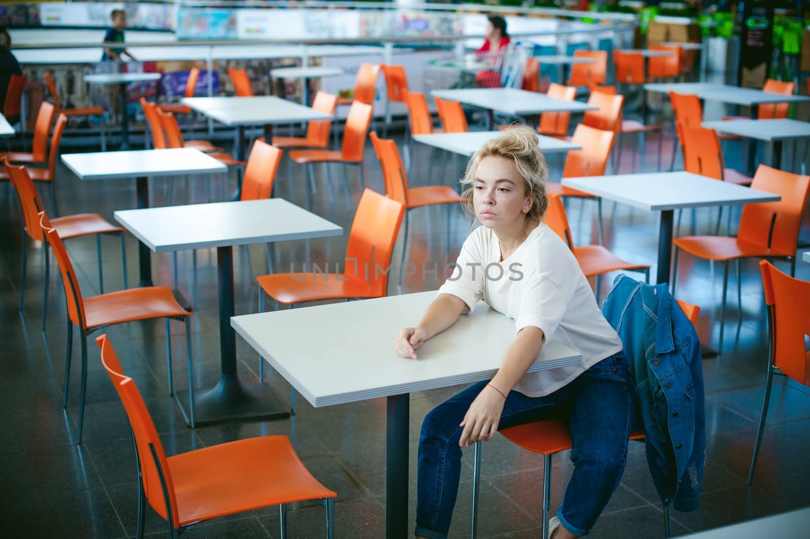 young beautiful woman in jeans clothes in business space of shopping center. portrait of a girl with freckles on her face, stylish girl in an empty cafe