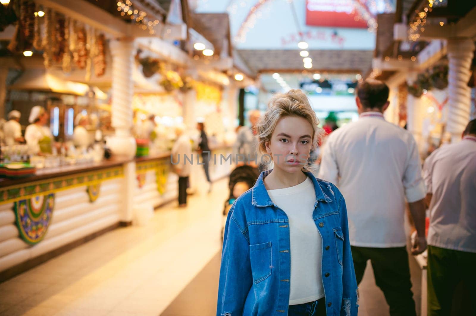young beautiful woman in jeans clothes in business space of shopping center. portrait of a girl with freckles on her face, stylish girl standing near show-windows of fair in shopping center