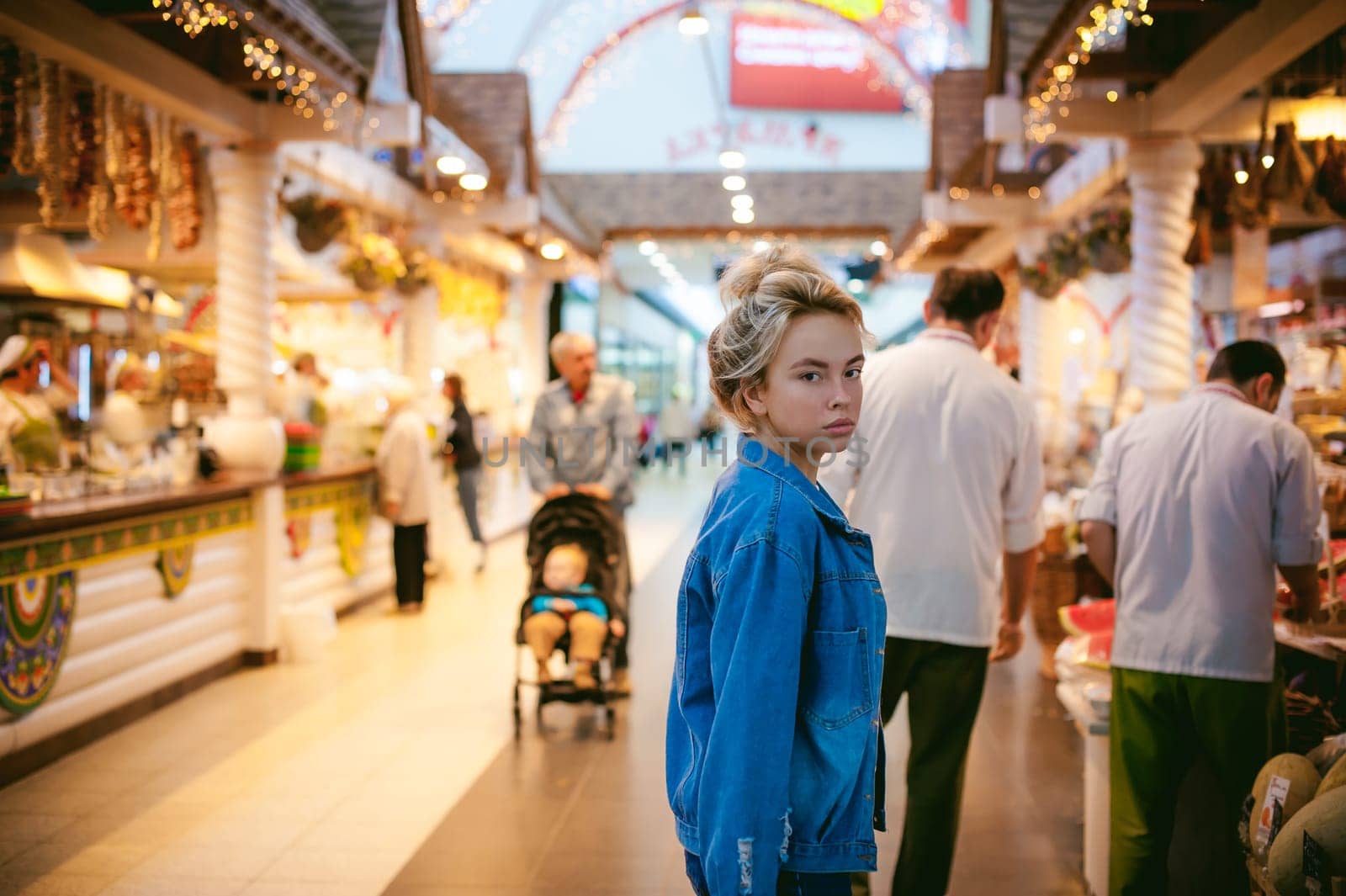 young beautiful woman in jeans clothes in business space of shopping center. portrait of a girl with freckles on her face, stylish girl standing near show-windows of fair in shopping center