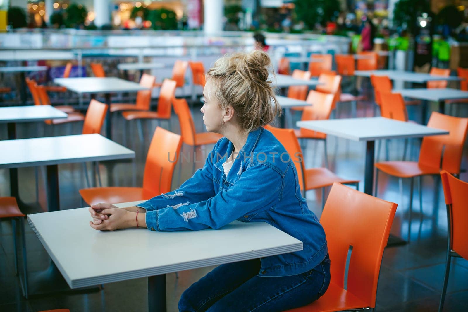 young beautiful woman in jeans clothes in business space of shopping center. portrait of a girl with freckles on her face, stylish girl in an empty cafe