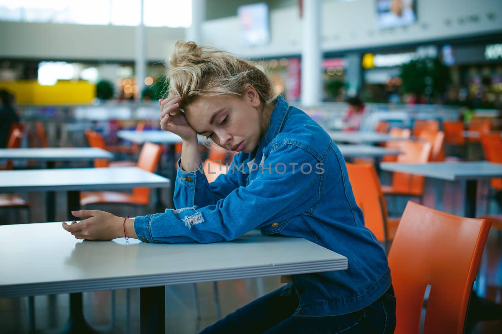 young beautiful woman in jeans clothes in business space of shopping center. portrait of a girl with freckles on her face, stylish girl in an empty cafe