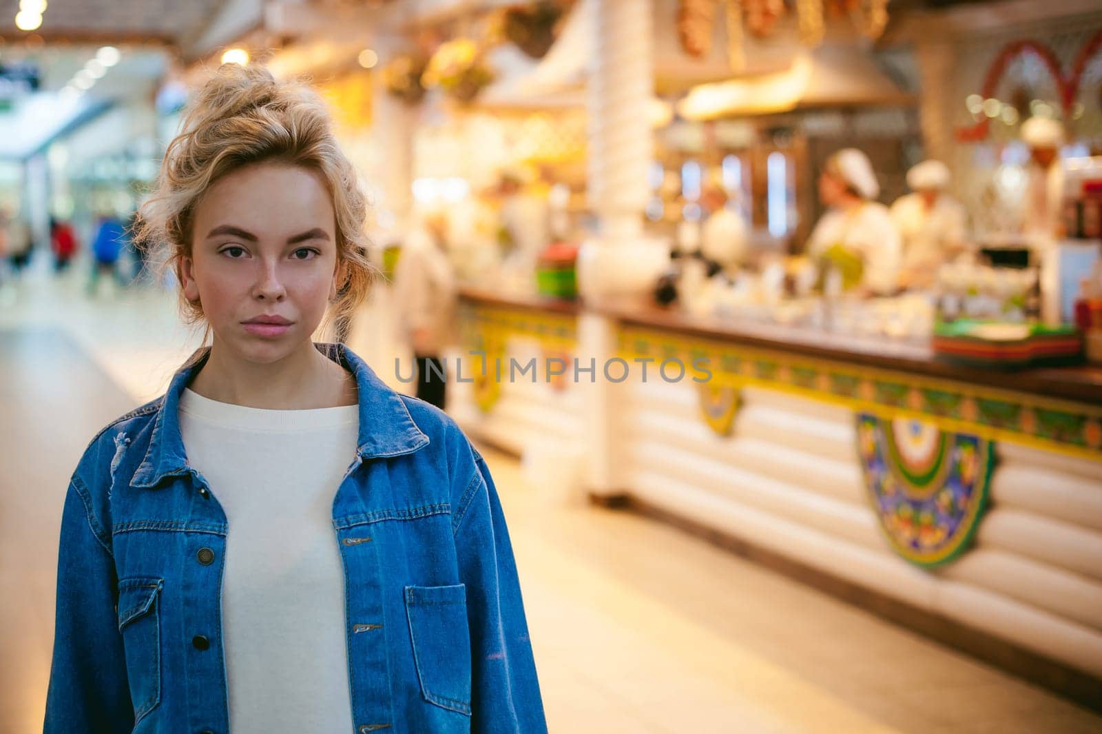 young beautiful woman in jeans clothes in business space of shopping center. portrait of a girl with freckles on her face, stylish girl standing near show-windows of fair in shopping center