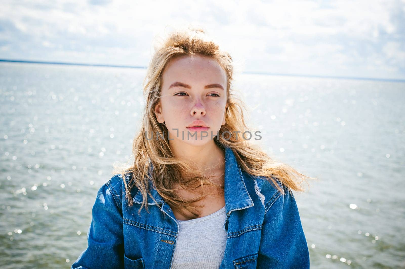 young beautiful woman in jeans clothes outdoors. portrait of a girl with freckles on her face, stylish girl on sea beach, on a sunny summer autumn day.
