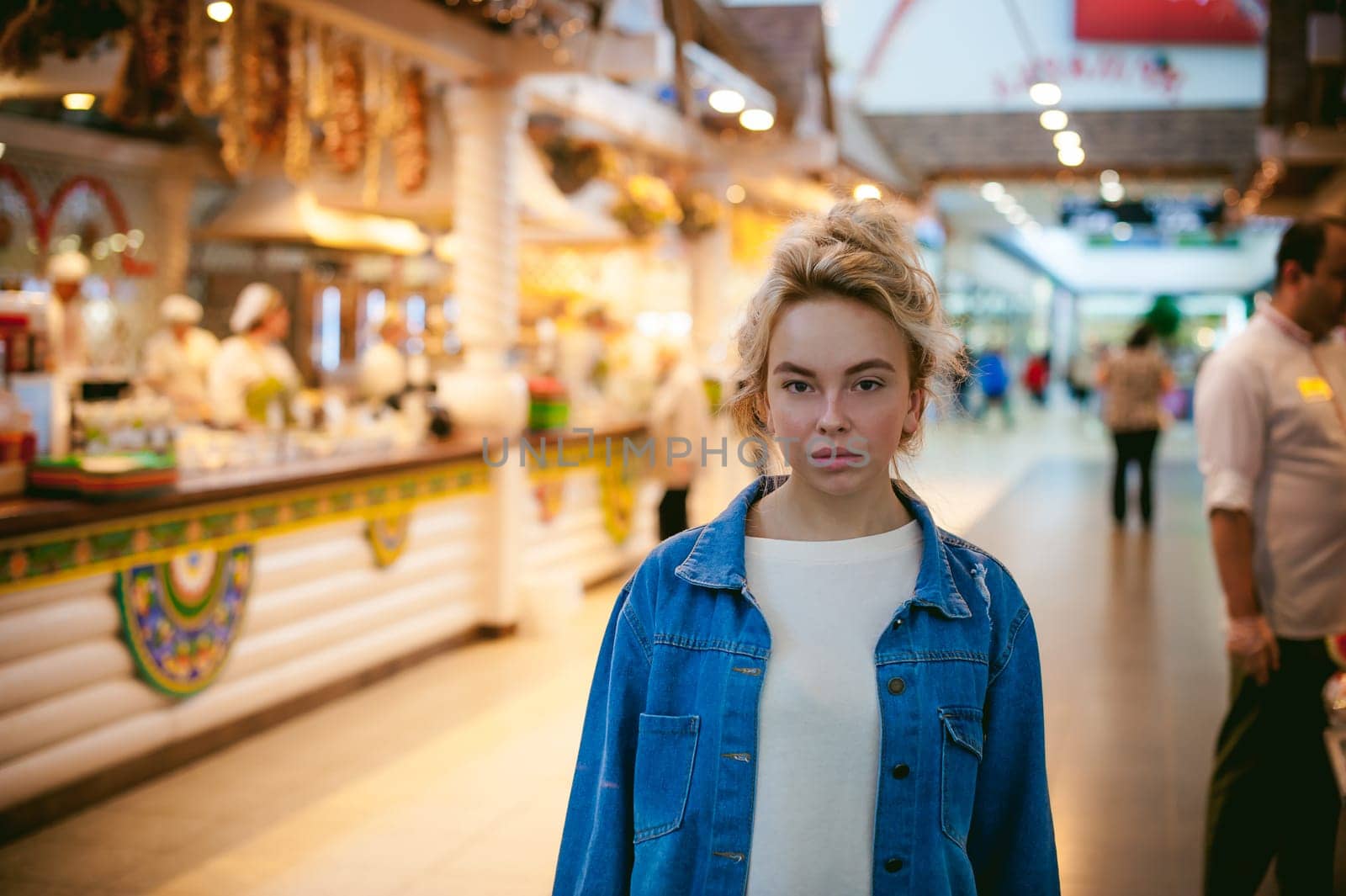 young beautiful woman in jeans clothes in business space of shopping center. portrait of a girl with freckles on her face, stylish girl standing near show-windows of fair in shopping center