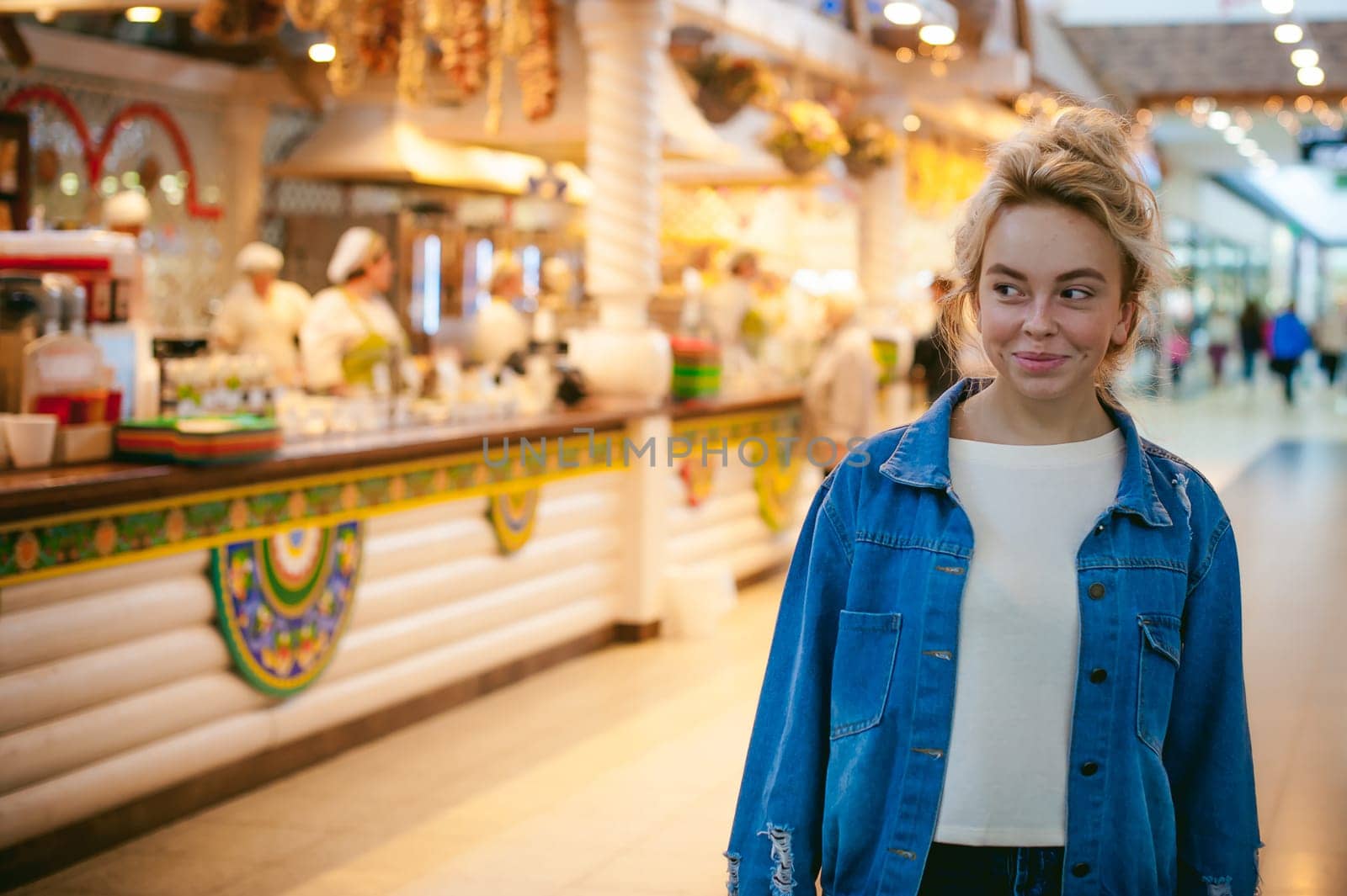 young beautiful woman in jeans clothes in business space of shopping center. portrait of a girl with freckles on her face, stylish girl standing near show-windows of fair in shopping center