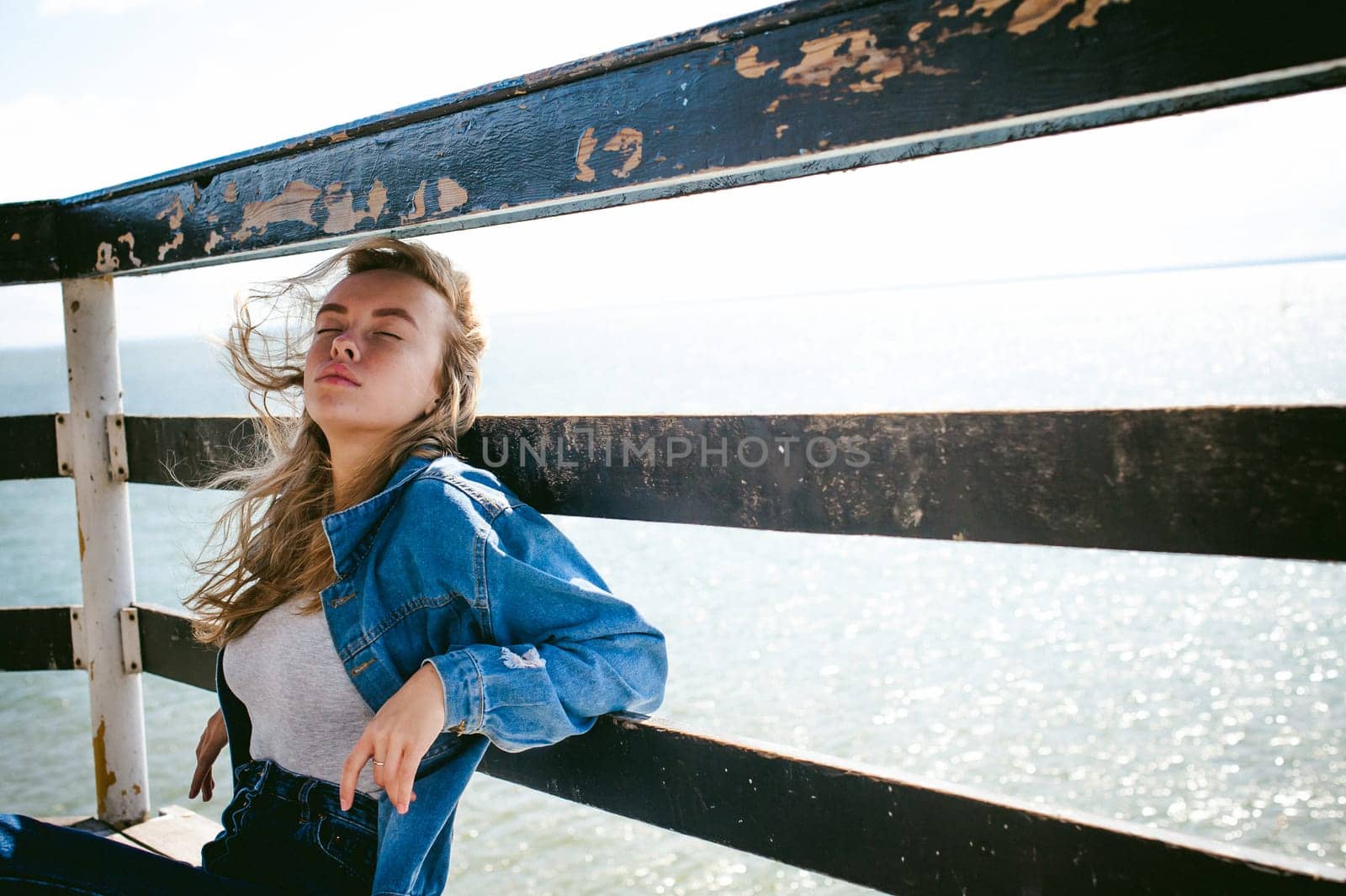young beautiful woman in jeans clothes outdoors. portrait of a girl with freckles on her face, stylish girl on sea beach rescue tower, on a sunny summer autumn day.