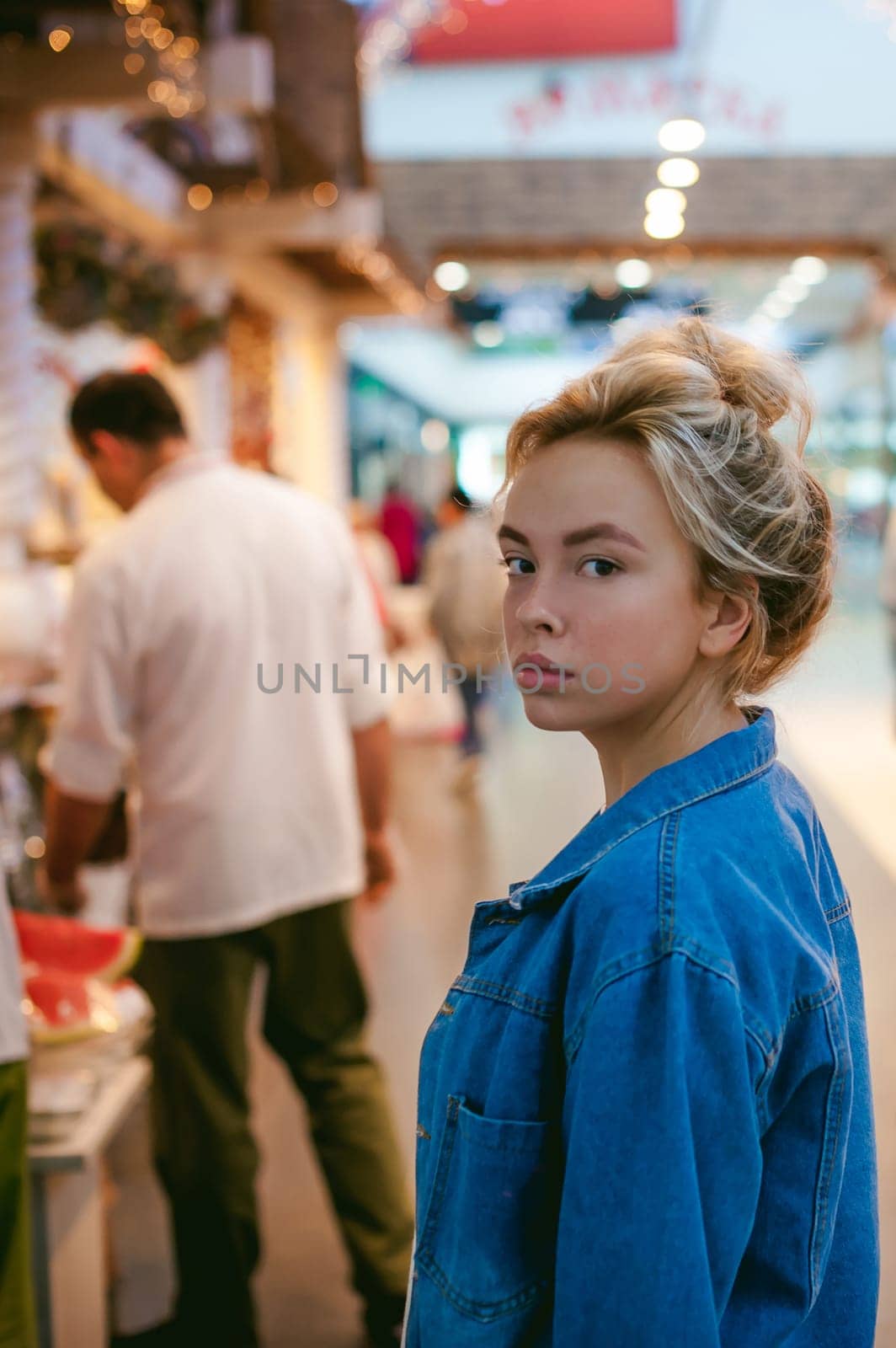 young beautiful woman in jeans clothes in business space of shopping center. portrait of a girl with freckles on her face, stylish girl standing near show-windows of fair in shopping center