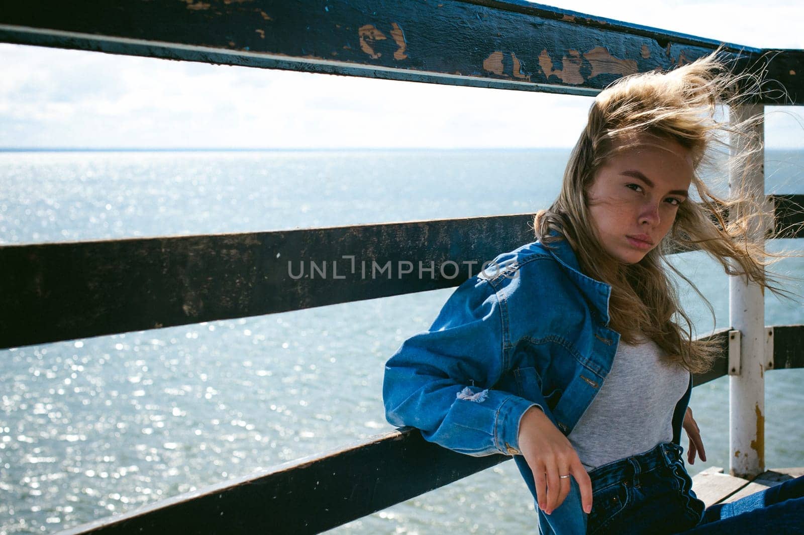 young beautiful woman in jeans clothes outdoors. portrait of a girl with freckles on her face, stylish girl on sea beach rescue tower, on a sunny summer autumn day.