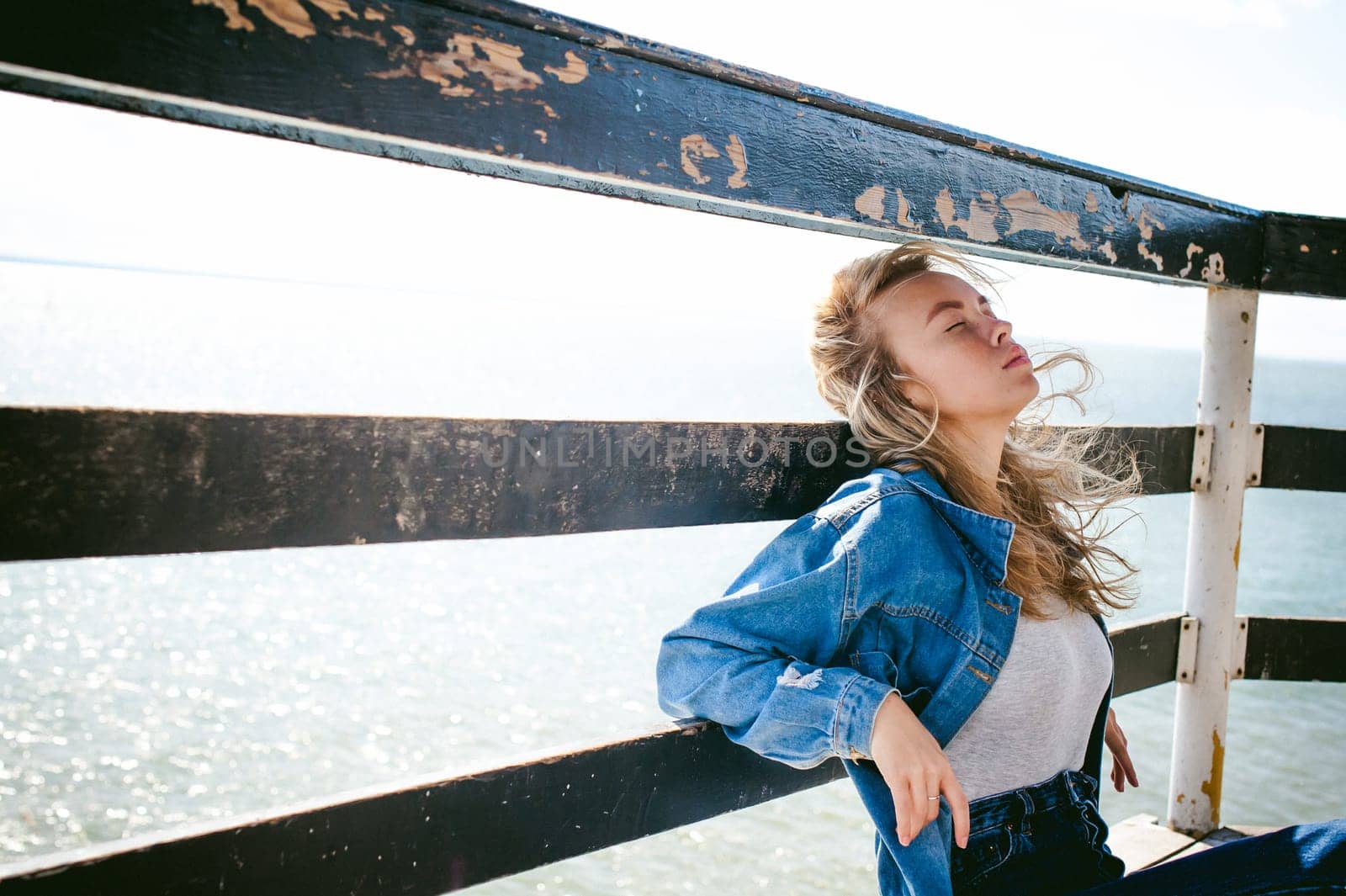 young beautiful woman in jeans clothes outdoors. portrait of a girl with freckles on her face, stylish girl on sea beach rescue tower, on a sunny summer autumn day.