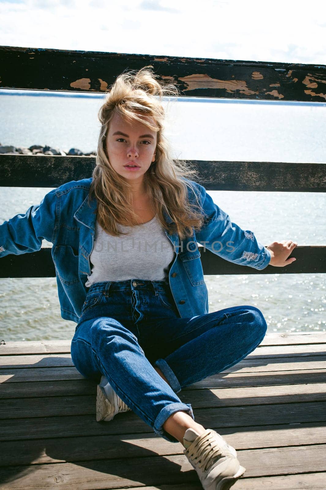 young beautiful woman in jeans clothes outdoors. portrait of a girl with freckles on her face, stylish girl on sea beach rescue tower, on a sunny summer autumn day.